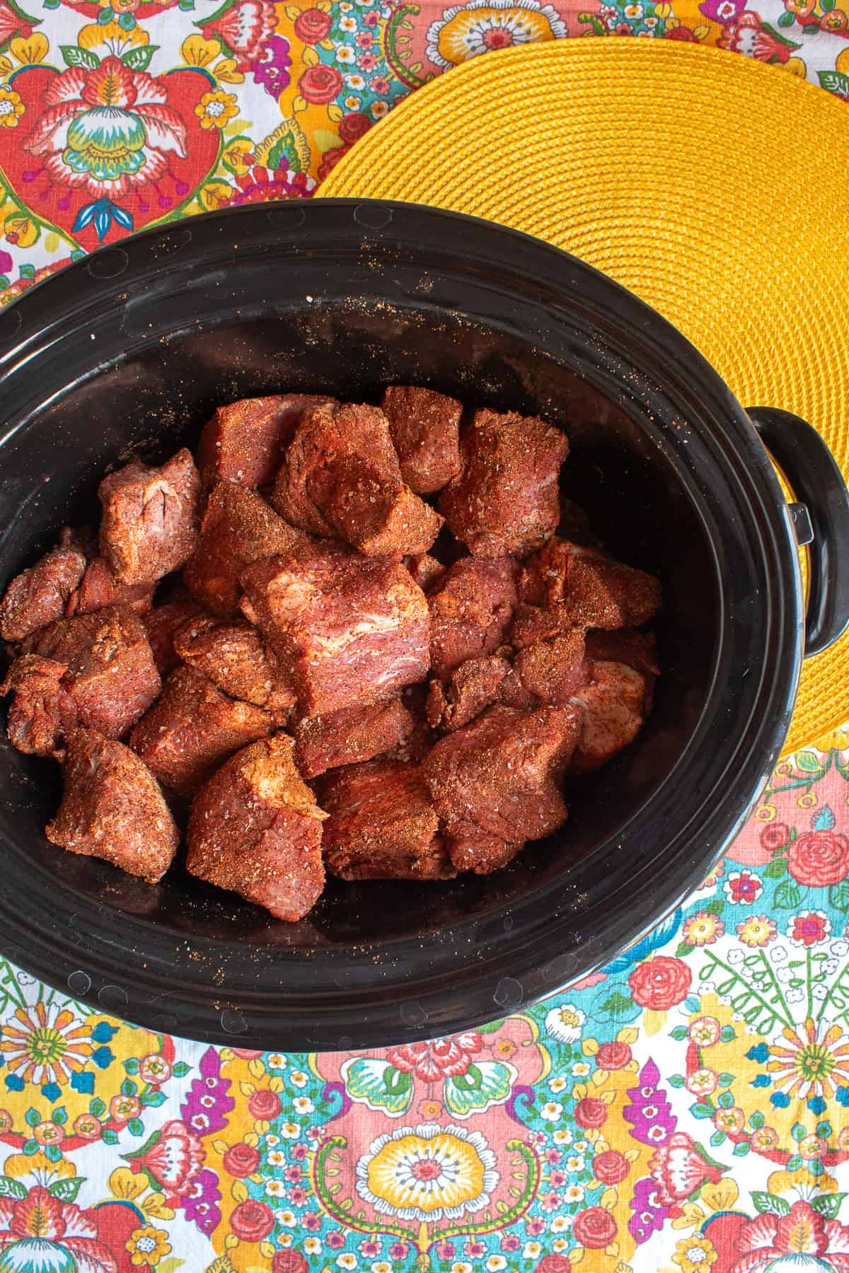 The cubes of beef are coated with the spice rub in the slow cooker crock.