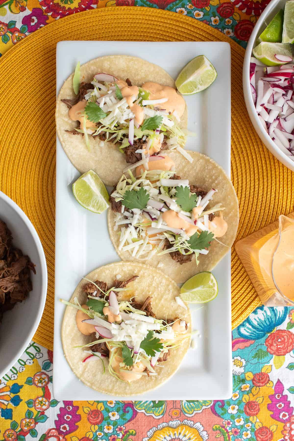 Three tacos are built on corn tortillas spread out on a white rectangular platter.
