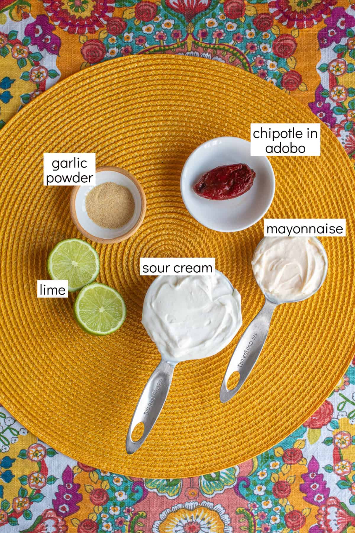 Ingredients for the chipotle crema are displayed on a yellow surface and have white text box labels including garlic powder, chipotle in adobo, mayonnaise, sour cream, and lime.
