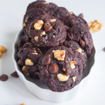 The baked cookies are stacked in a shallow white dish and the detail image highlights golden walnut pieces and soft chocolate chips in a dark brown cookie.