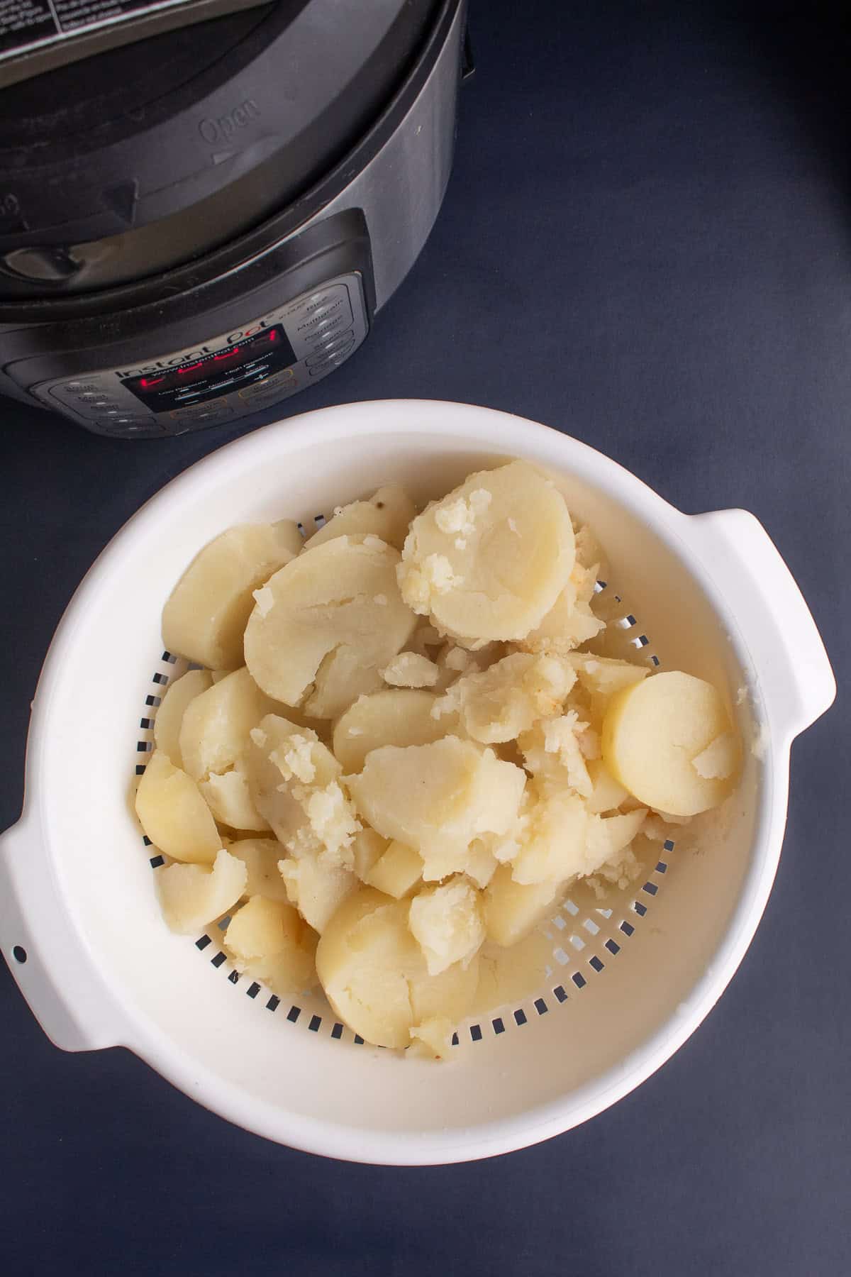 The cooked potatoes are drained in a white colander.