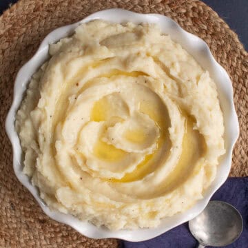 Fluffy mashed potatoes are swirled in a white round serving dish and drizzled with melted butter.