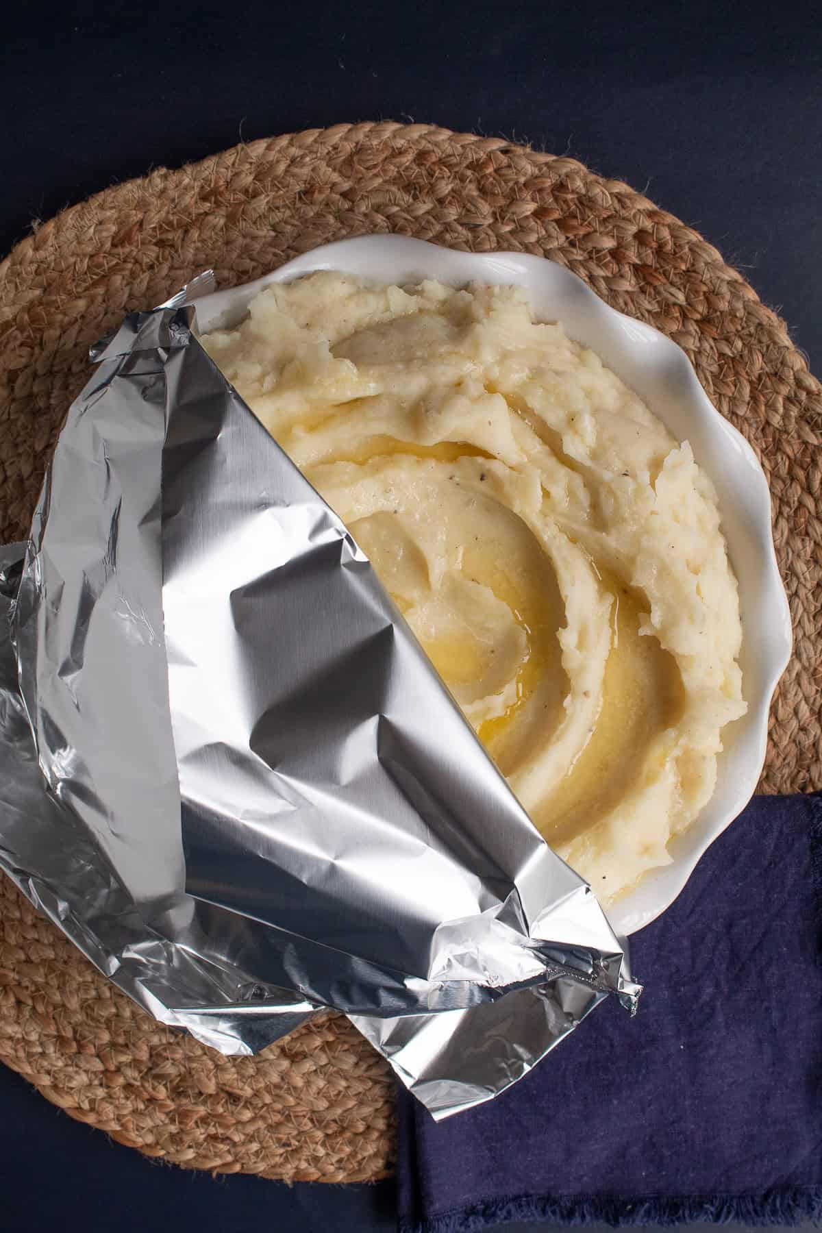 The platter of mashed potatoes is partially covered with a sheet of foil.