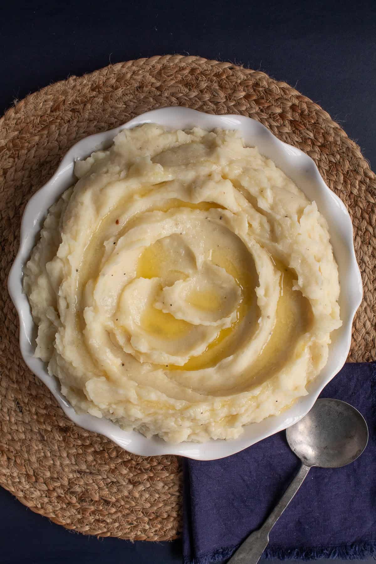 Fluffy mashed potatoes are swirled in a white round serving dish and drizzled with melted butter.