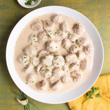 The meatballs and gravy are served in a large white platter and garnished with finely chopped chives.
