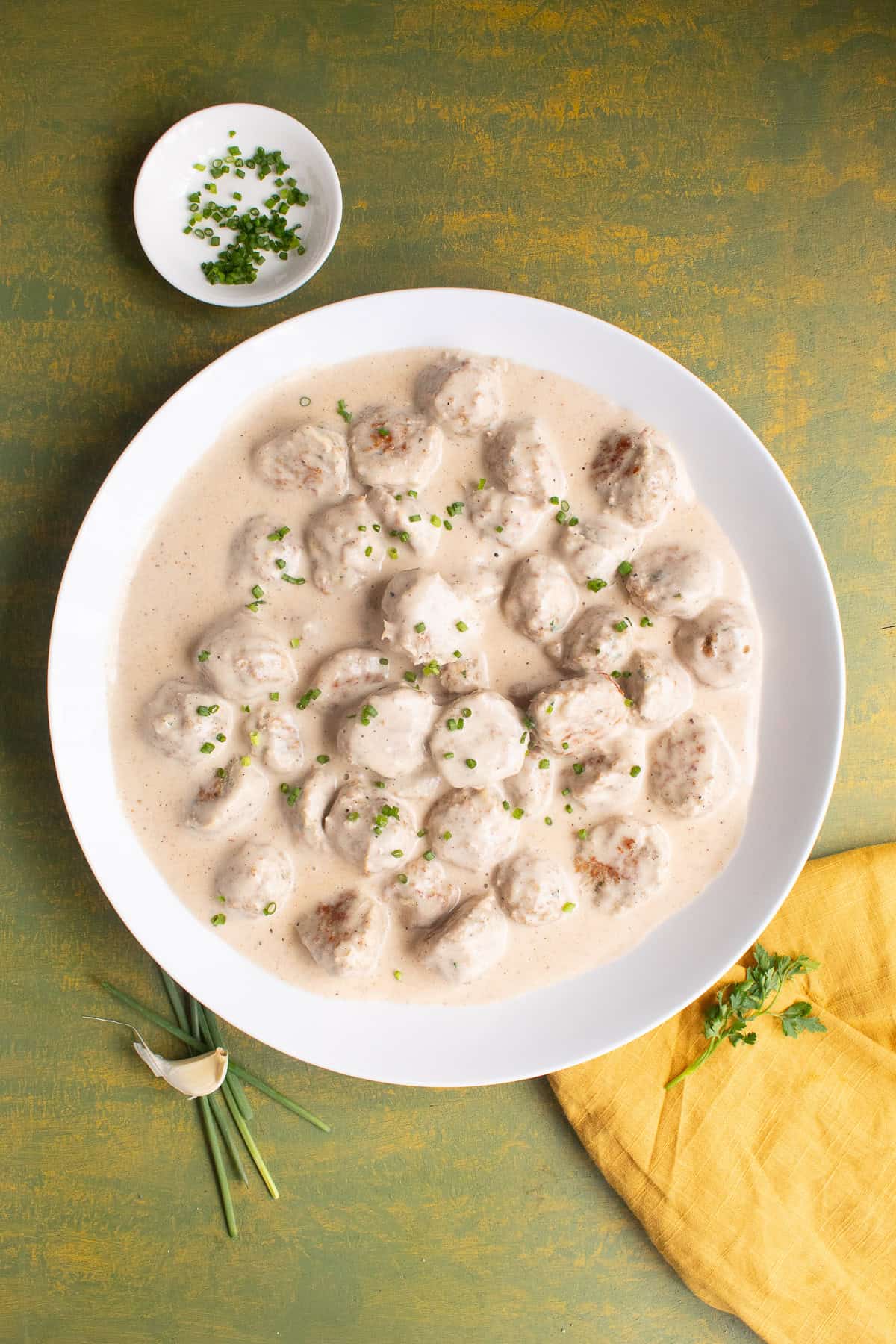 The meatballs and gravy are served in a large white platter and garnished with finely chopped chives.
