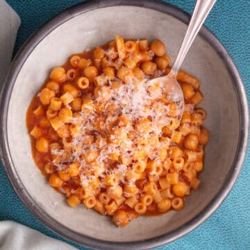 A gray bowl is piled with a orange-red pasta with chickpeas and grated Parmesan cheese.