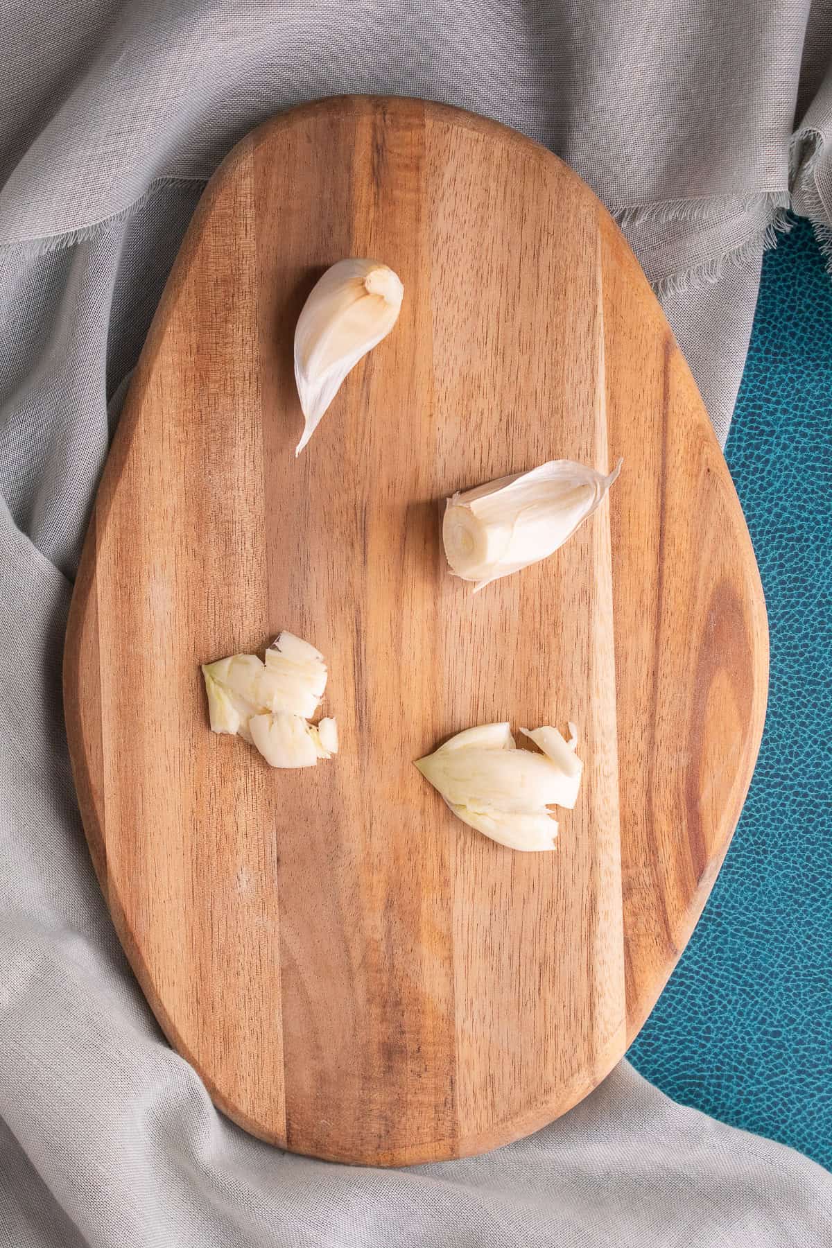 Garlic is prepared on a small wooden cutting board by first cutting off the end, then removing the skin, and finally crushing flat.