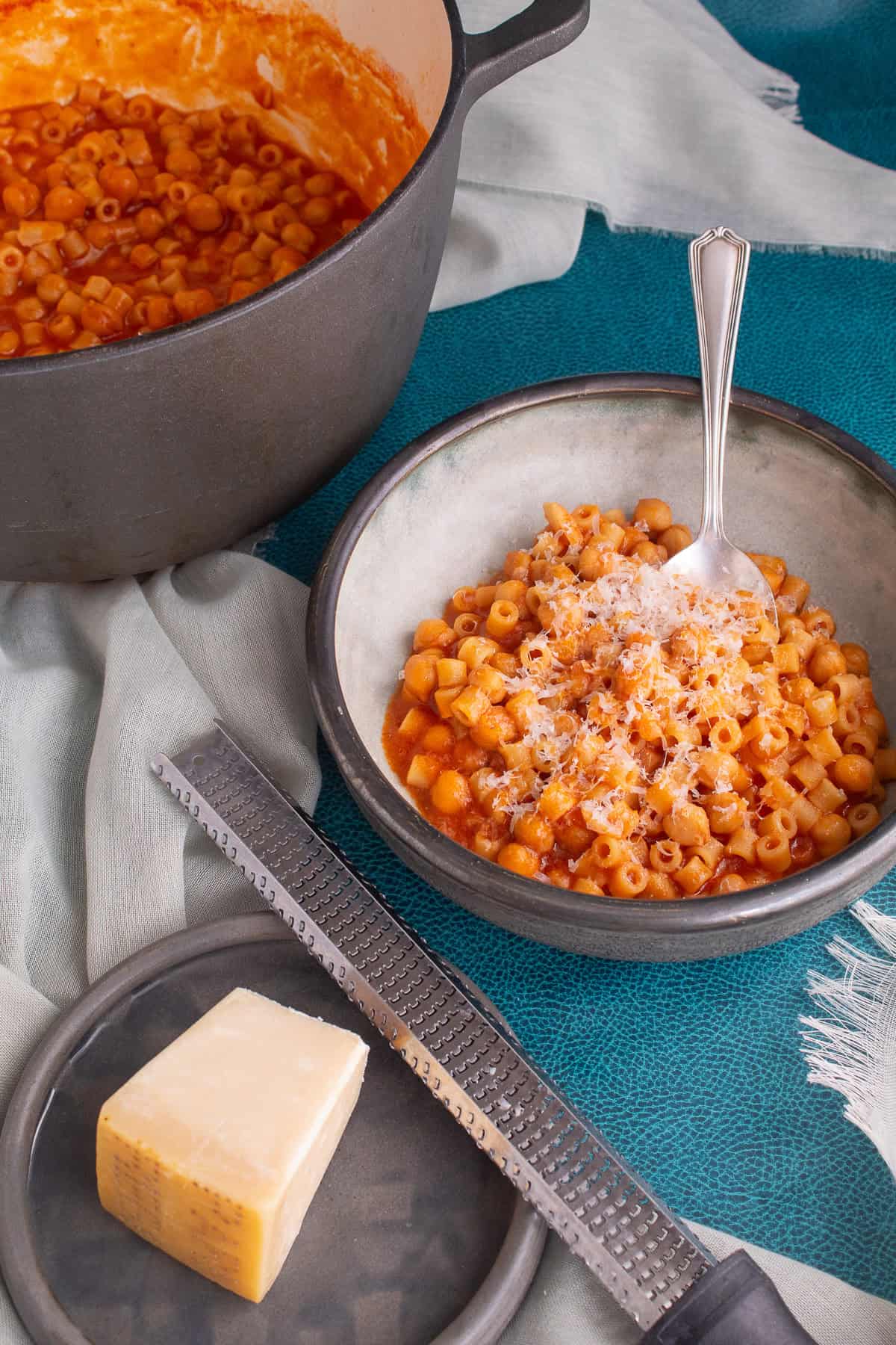 A gray bowl holds a portion of the pasta e ceci that has been sprinkled with grated Parmesan cheese.