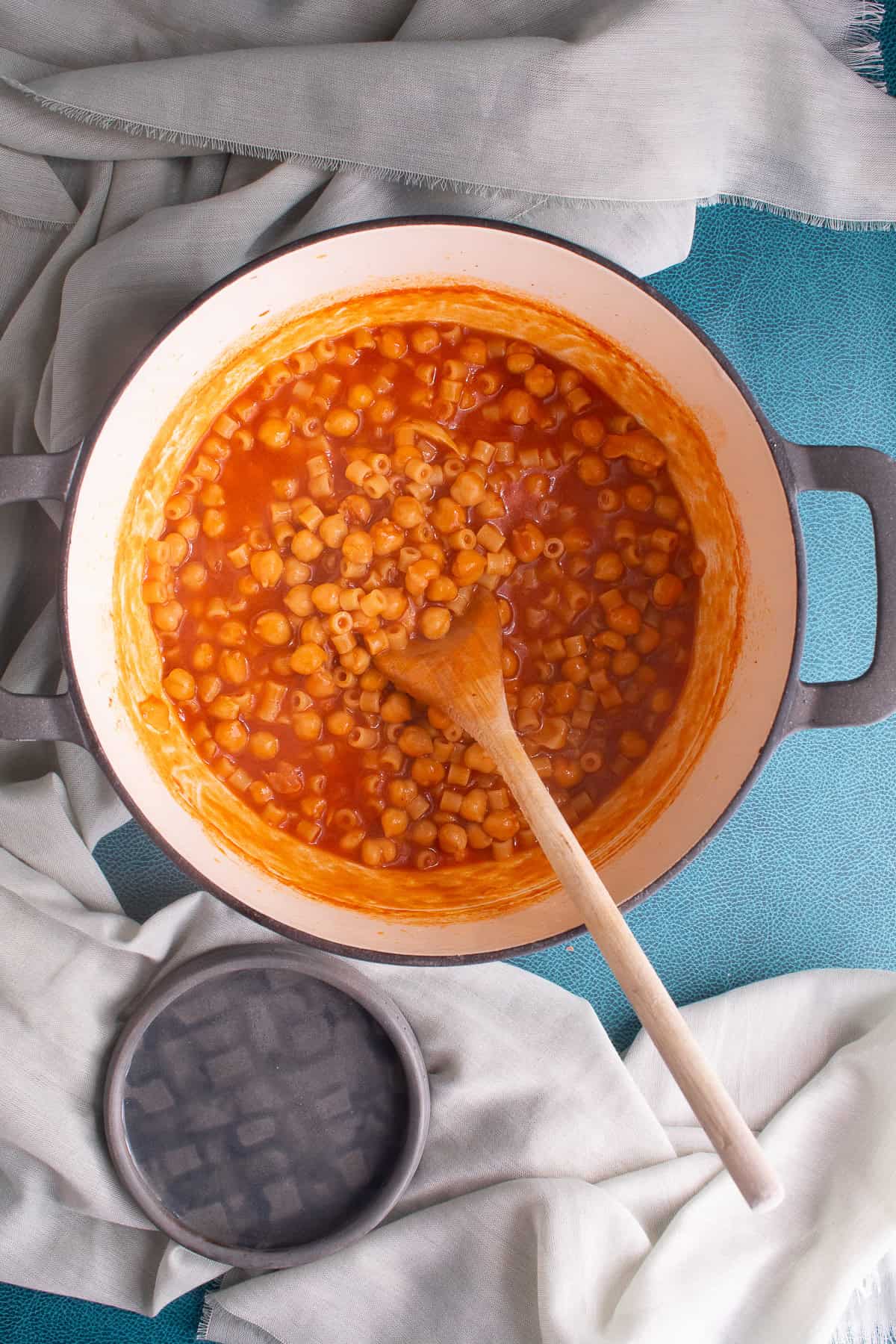 The chickpeas and pasta are in a thickened tomato sauce stirred with a wooden spoon.