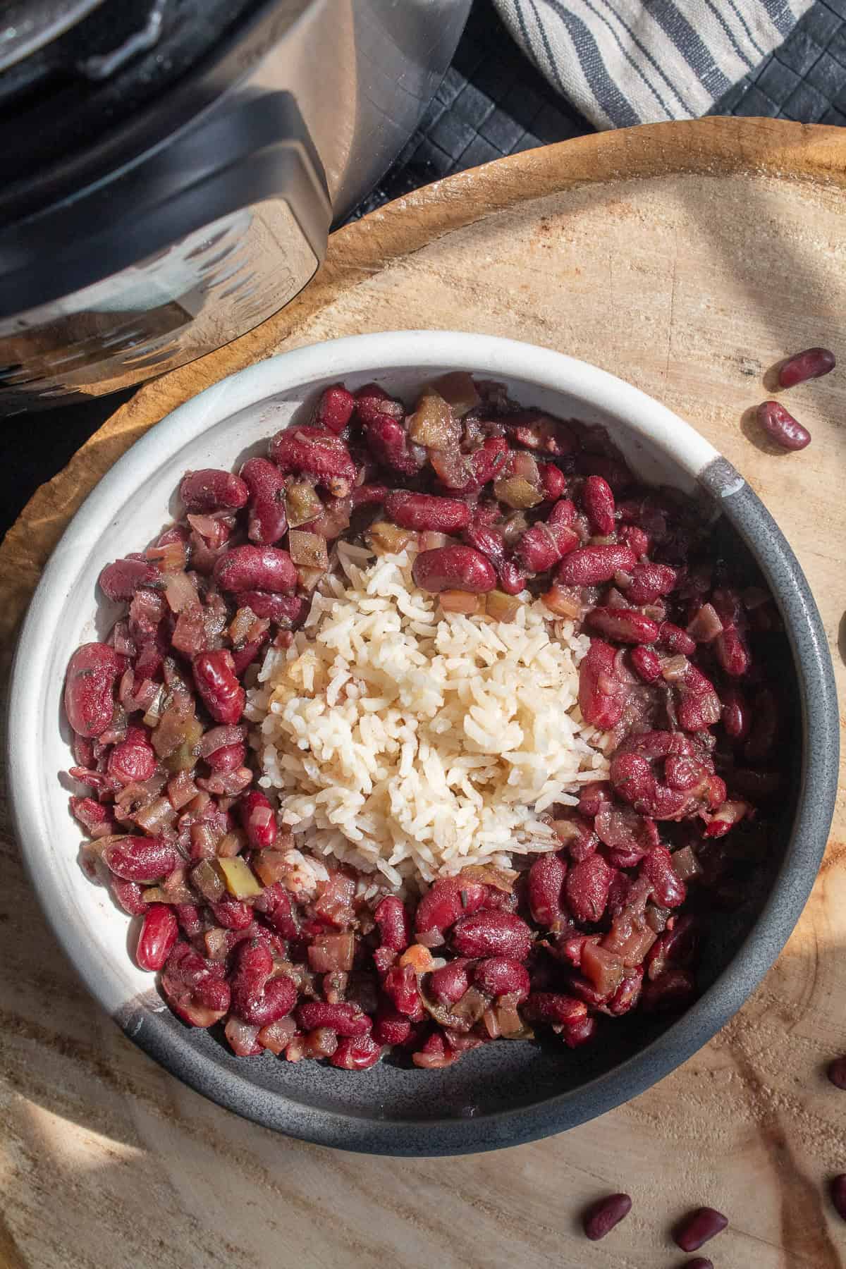 A bowl of red beans and rice sits on a wooden background alongside a pressure cooker.