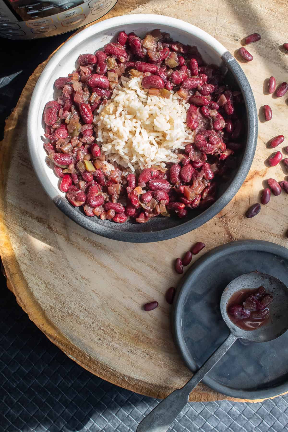 A bowl of red beans and rice sits on a wooden background alongside a spoon of cooked beans.