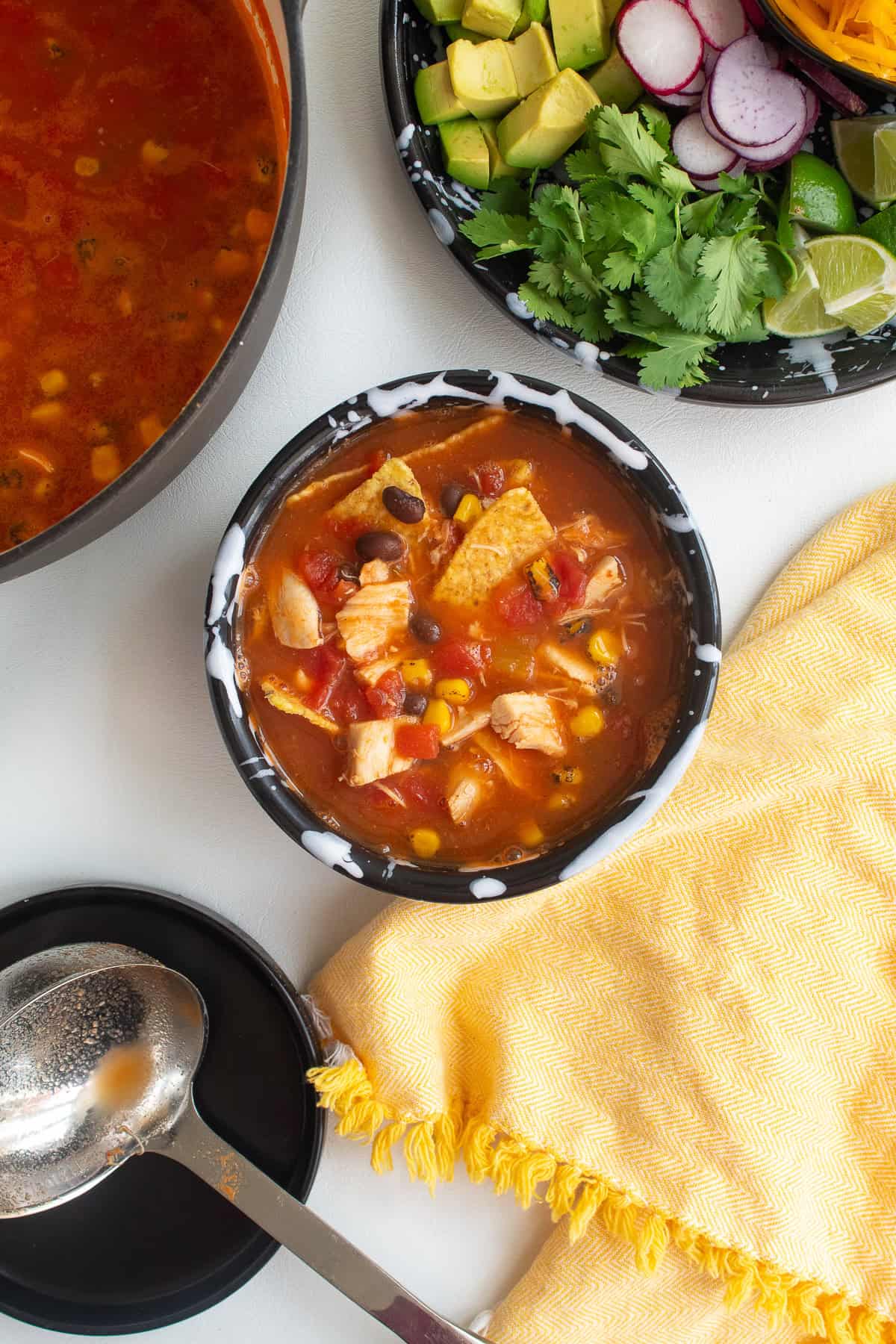 The soup is ladled over the chips in the bowl and black beans, chicken, corn, and tomato pieces are visible.
