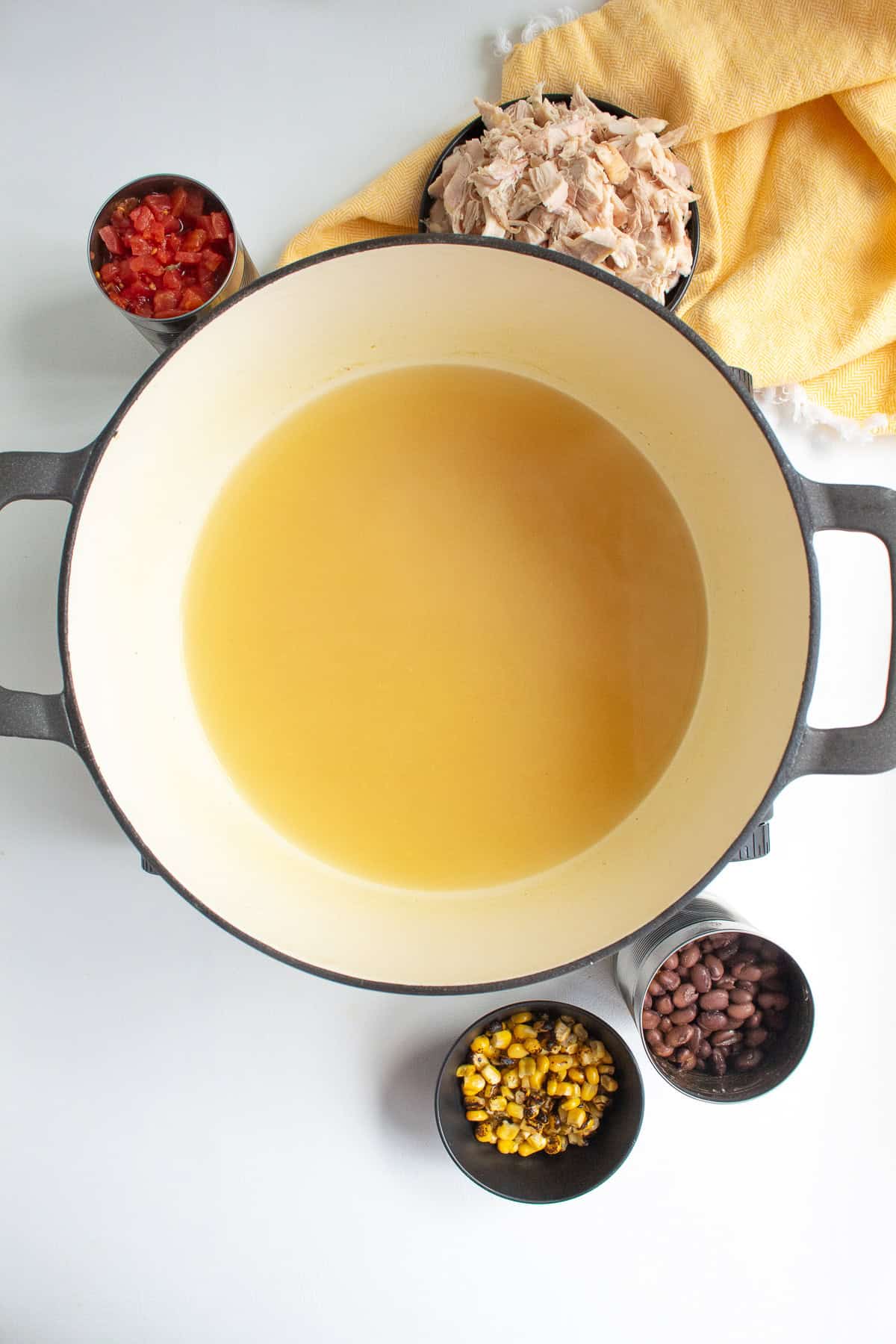 Chicken stock is heated in the bottom of a large pot which is surrounded by the canned ingredients and rotisserie chicken.