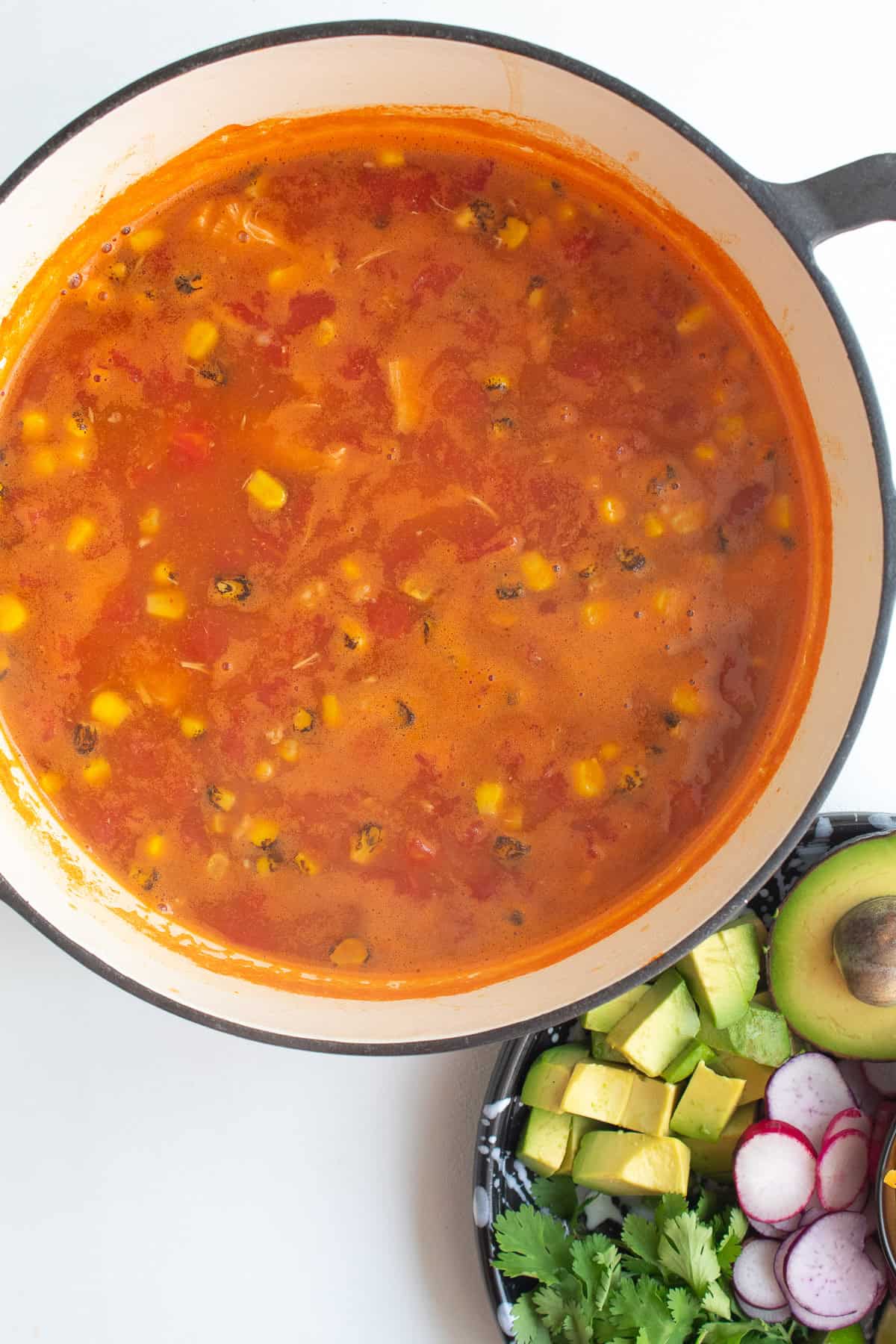 The completed soup has a bright red-orange color and visible bits of chicken, tomato, black bean, and chicken.