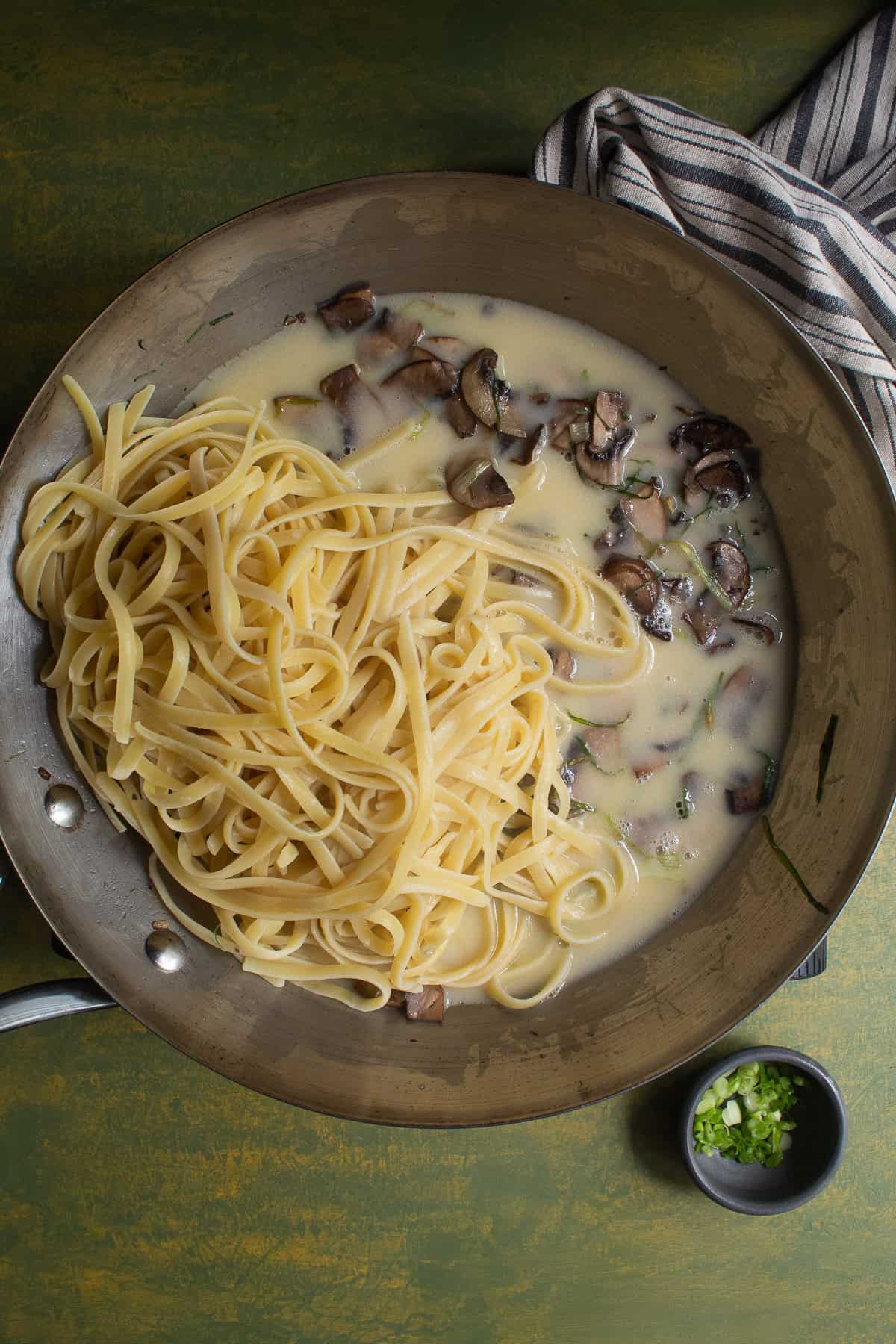 Pasta, sauteed mushrooms, and a pale yellow sauce are combined in a skillet.