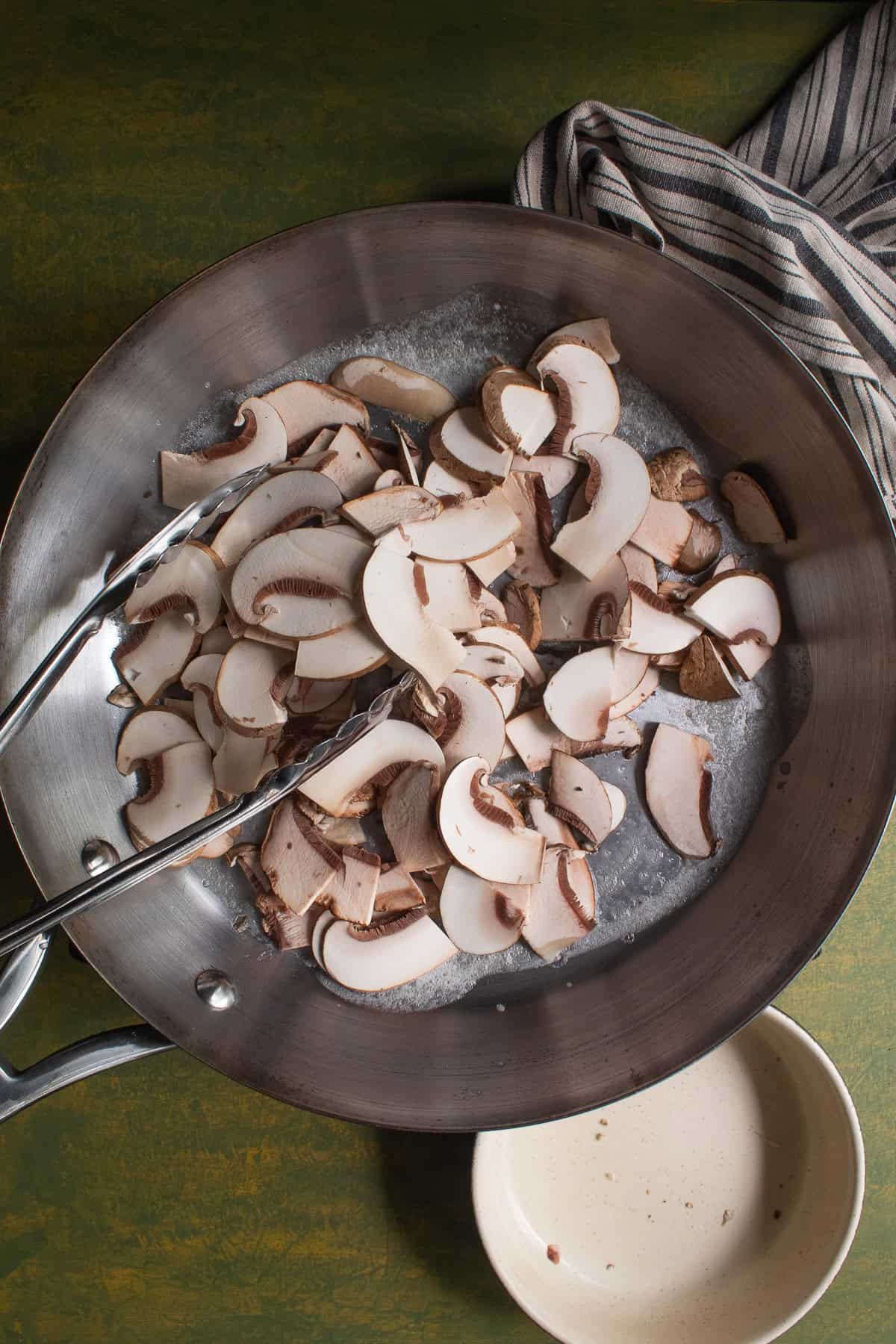 Thinly sliced mushrooms are added to a large skillet.
