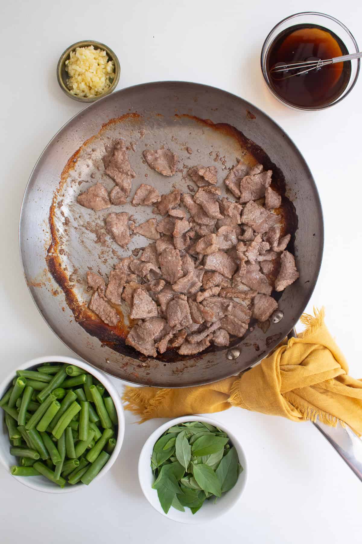 The browned beef is in a skillet surrounded by other stir fry ingredients.