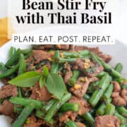 A white bowl of stir fried beef, green beans, garlic, and Thai basil leaves. A text box at the top of the image contains the words, "beef and green bean stir fry with Thai basil" and " plan. eat. post. repeat."
