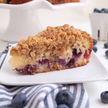 A detail image of a slice of coffee cake shows burst purple blueberries under a layer of golden oat crumble.