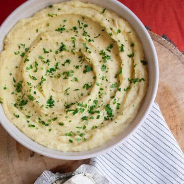 Mashed potatoes swirled in a white bowl and garnished with finely chopped parsley.