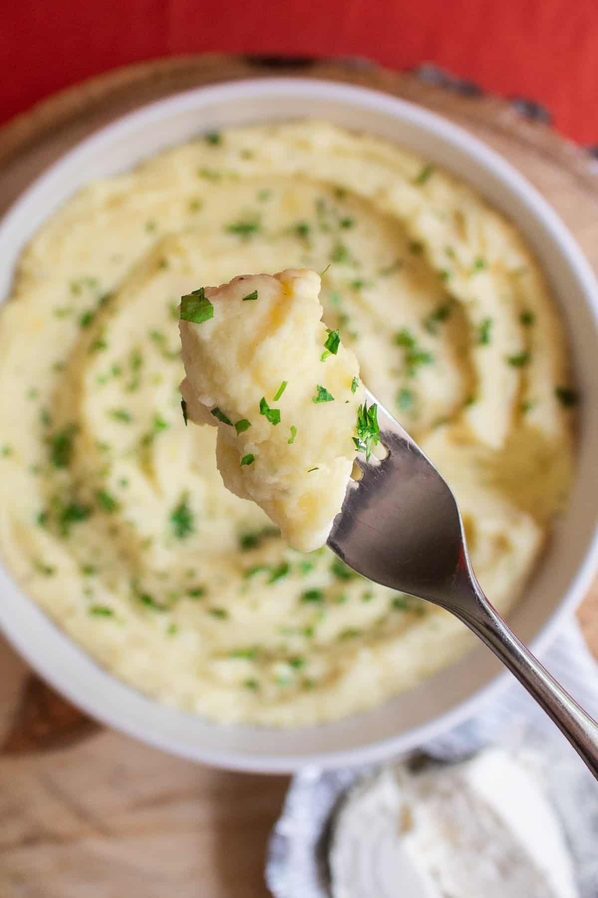 A forkful of potatoes over the serving bowl.