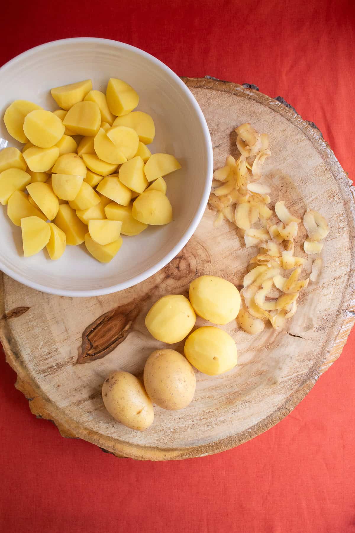 Yellow potatoes are peeled and cut into 2-inch pieces on a wooden cutting board.