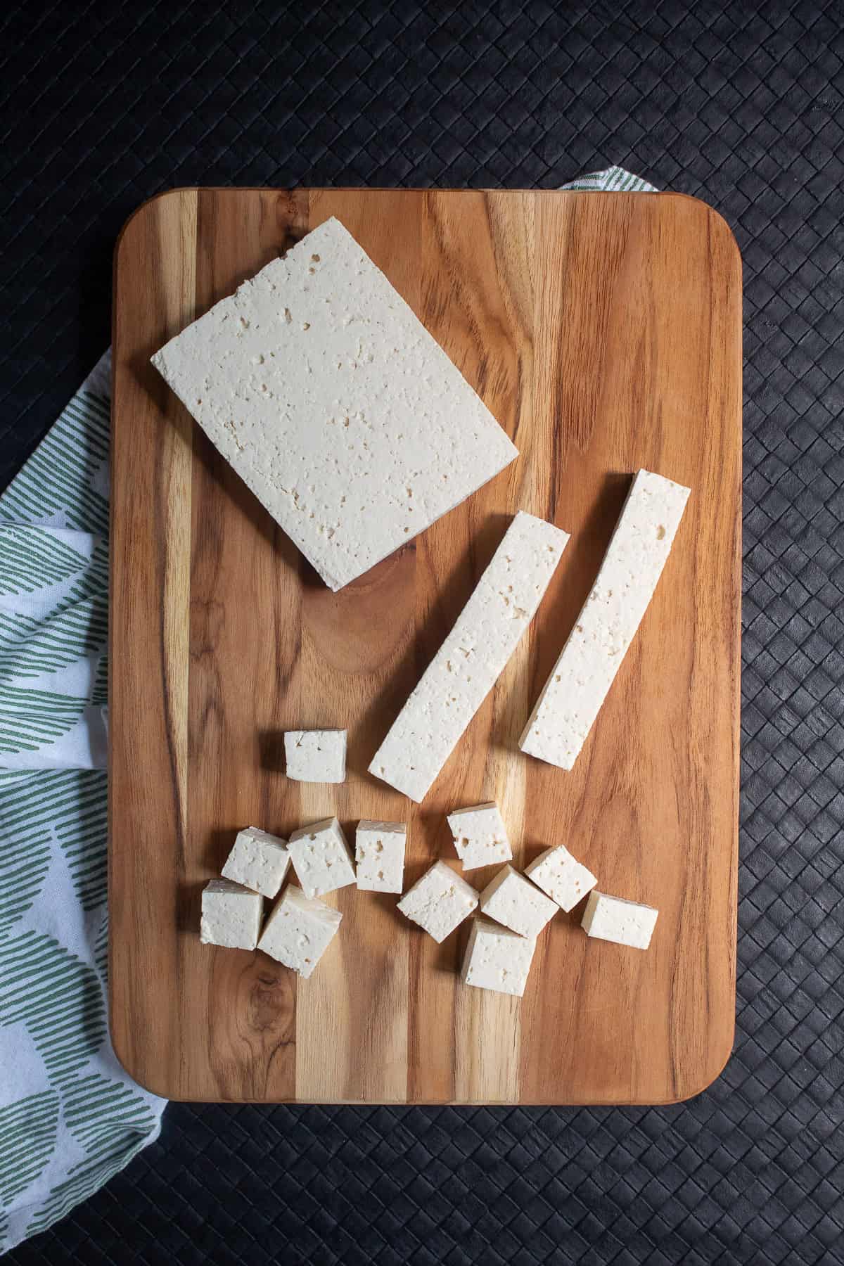 Tofu is cut into strips and cubes on a wooden cutting board.
