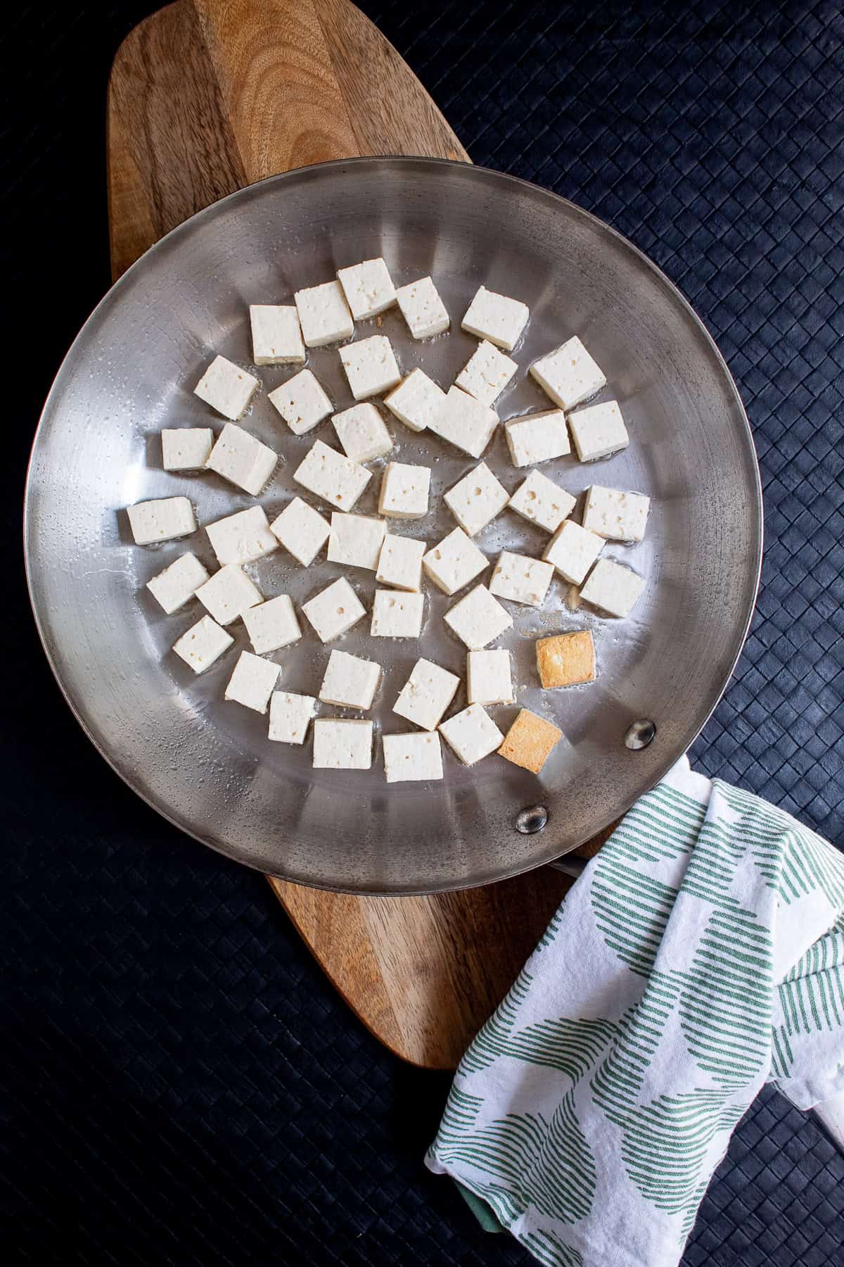 Tofu cubes are fried in the bottom of a skillet.