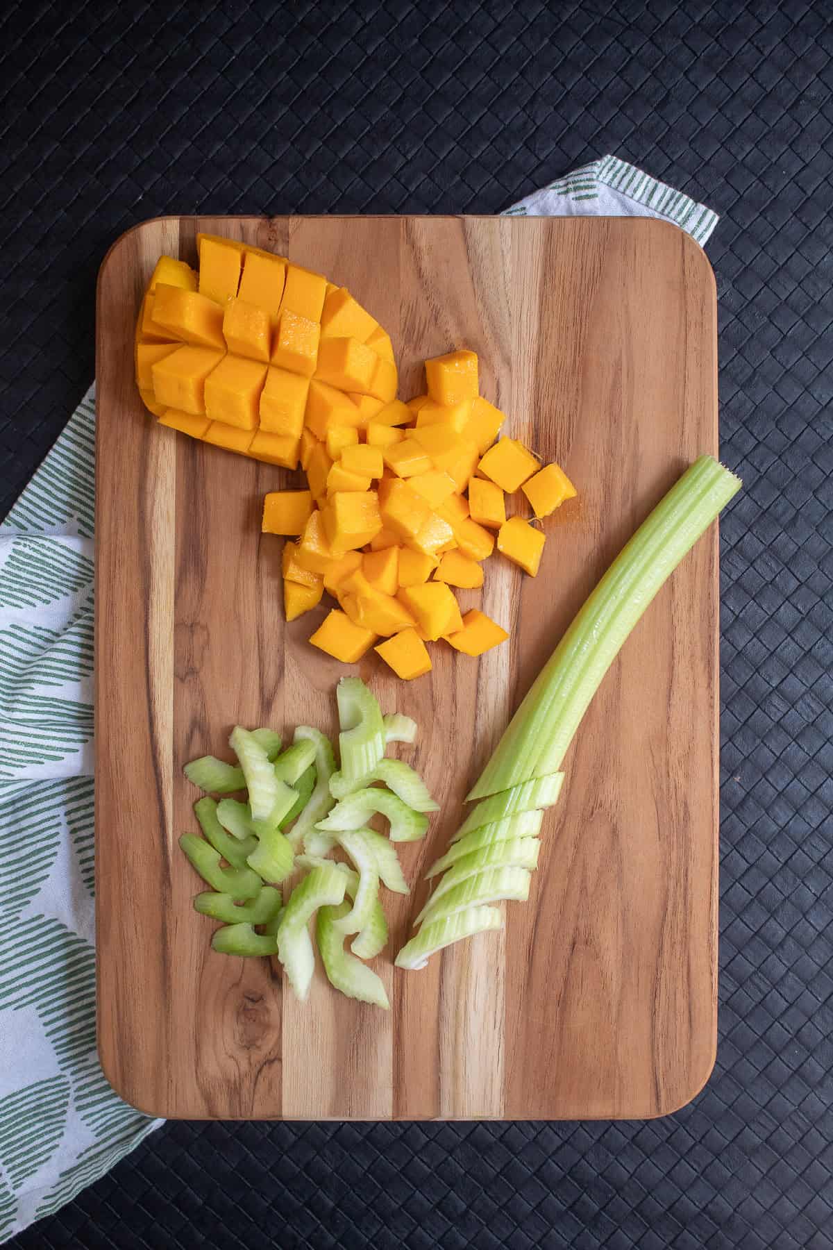 Mango and celery are prepared on a wooden cutting board.
