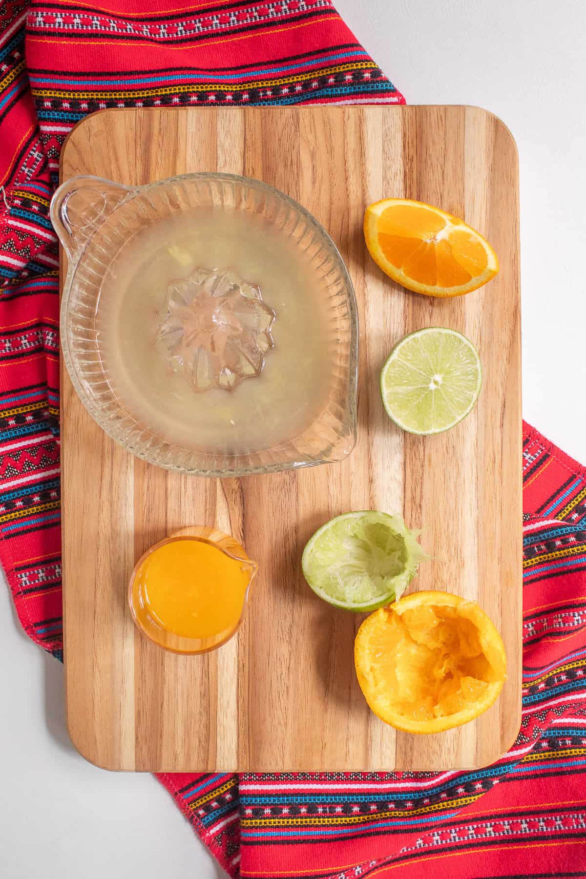 Orange and lime are juiced on a wooden cutting board.
