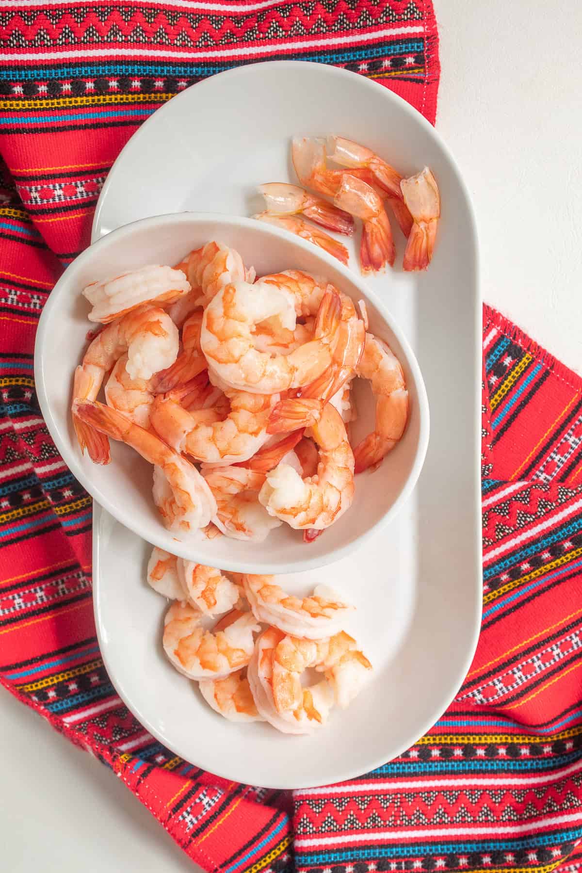 Cooked shrimp in a bowl in process of removing the tails.