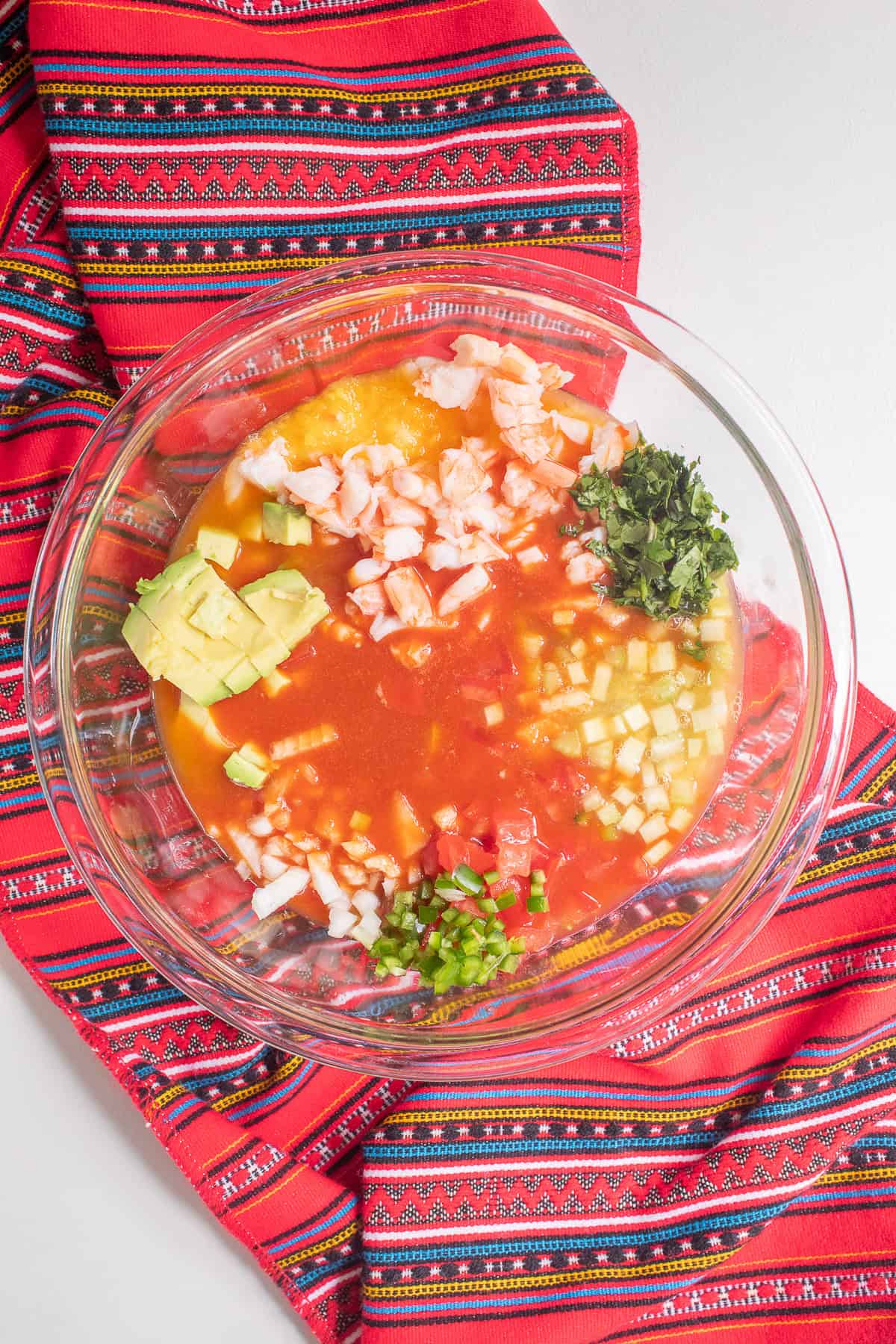 Tomato, lime, and orange juice are added to the bowl of chopped vegetables and shrimp.