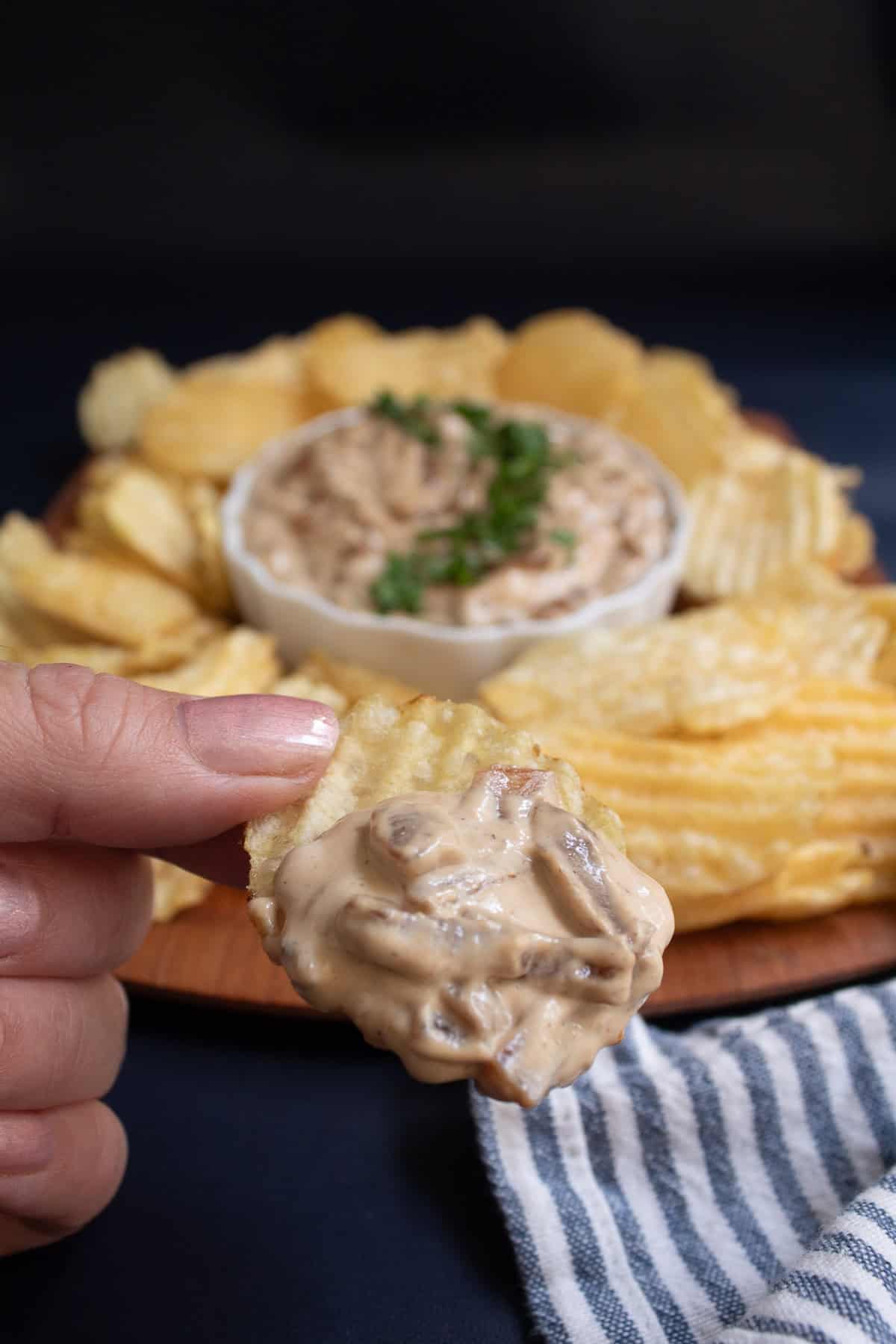 A hand is holding a chip with onion dip.