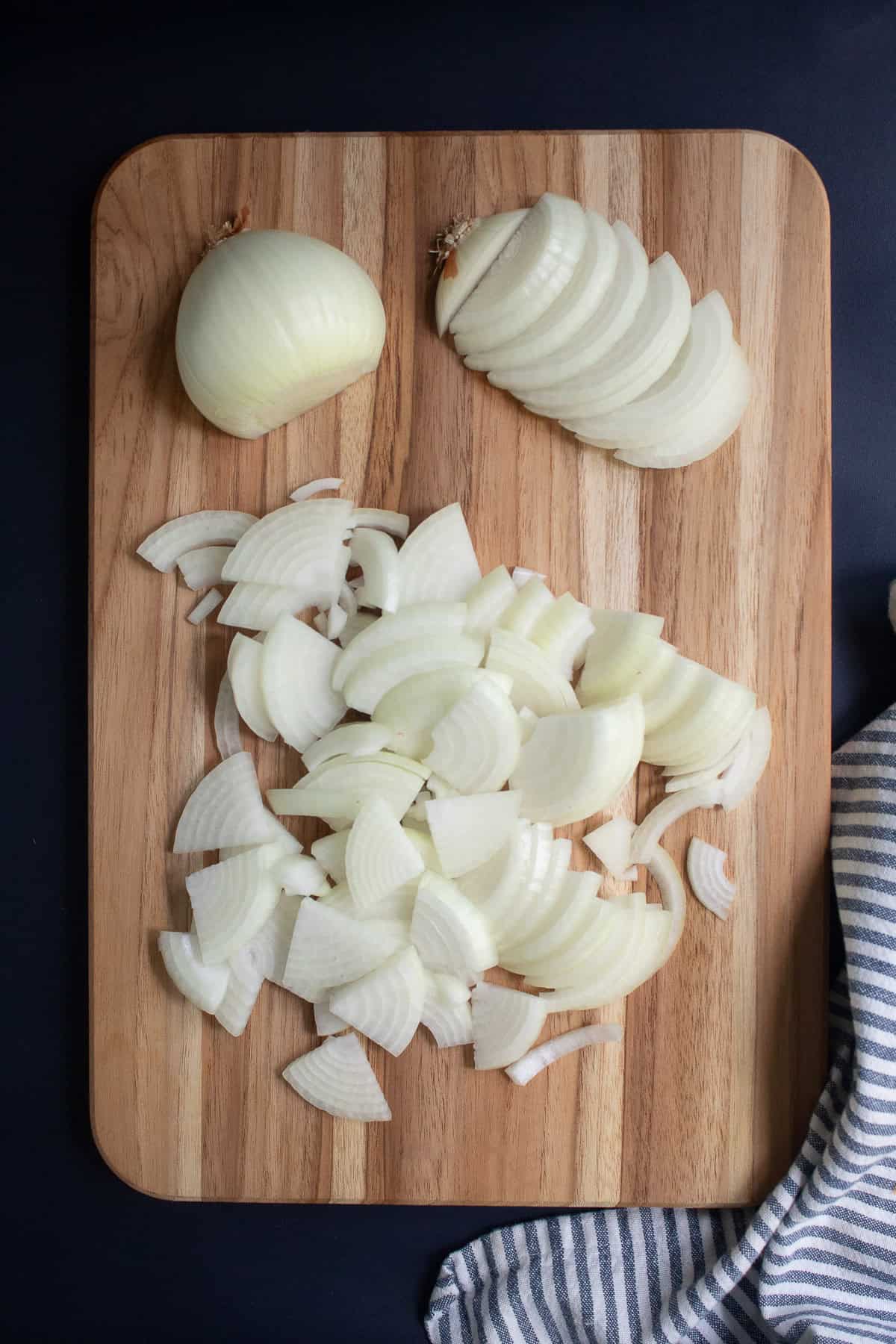 A wood cutting board has onions cut in half and in slices.