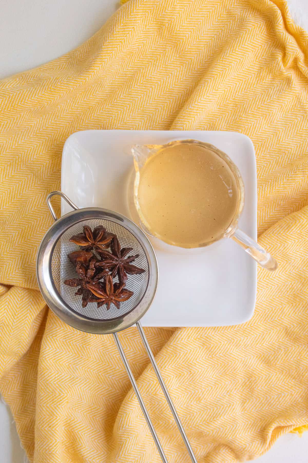 The star anise pods sit in a mesh strainer next to a small pitcher of syrup.