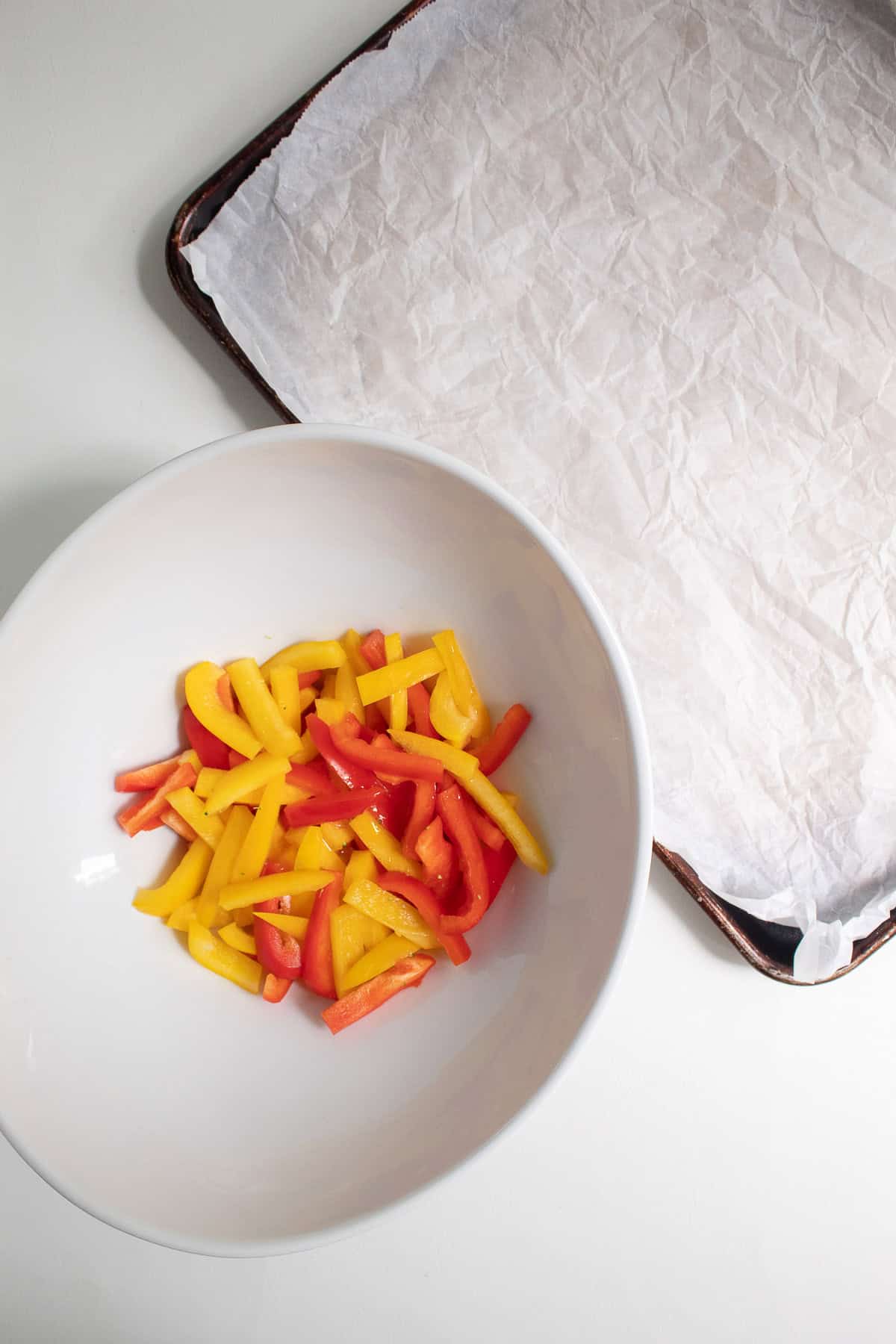 Bell pepper strips and vegetable oil are tossed together in a large white bowl.