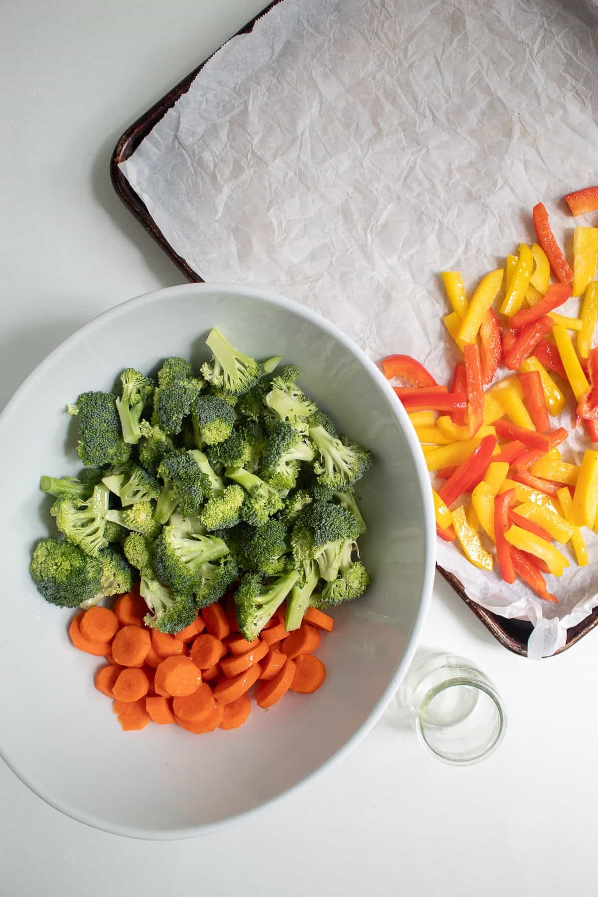 Broccoli and carrots are in a large white bowl along with a bit of vegetable oil.