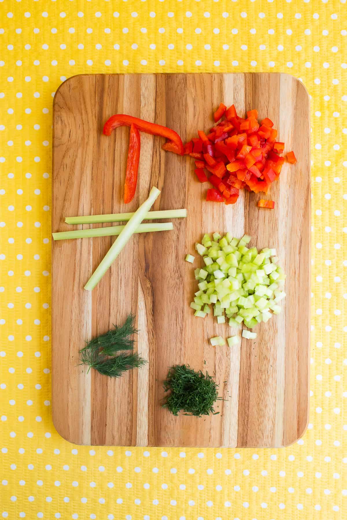 Bell pepper, celery, and dill are prepared on a wooden cutting board for the dish.