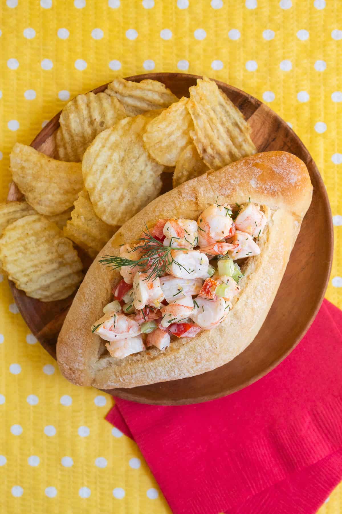 A shrimp roll is plated with potato chips.