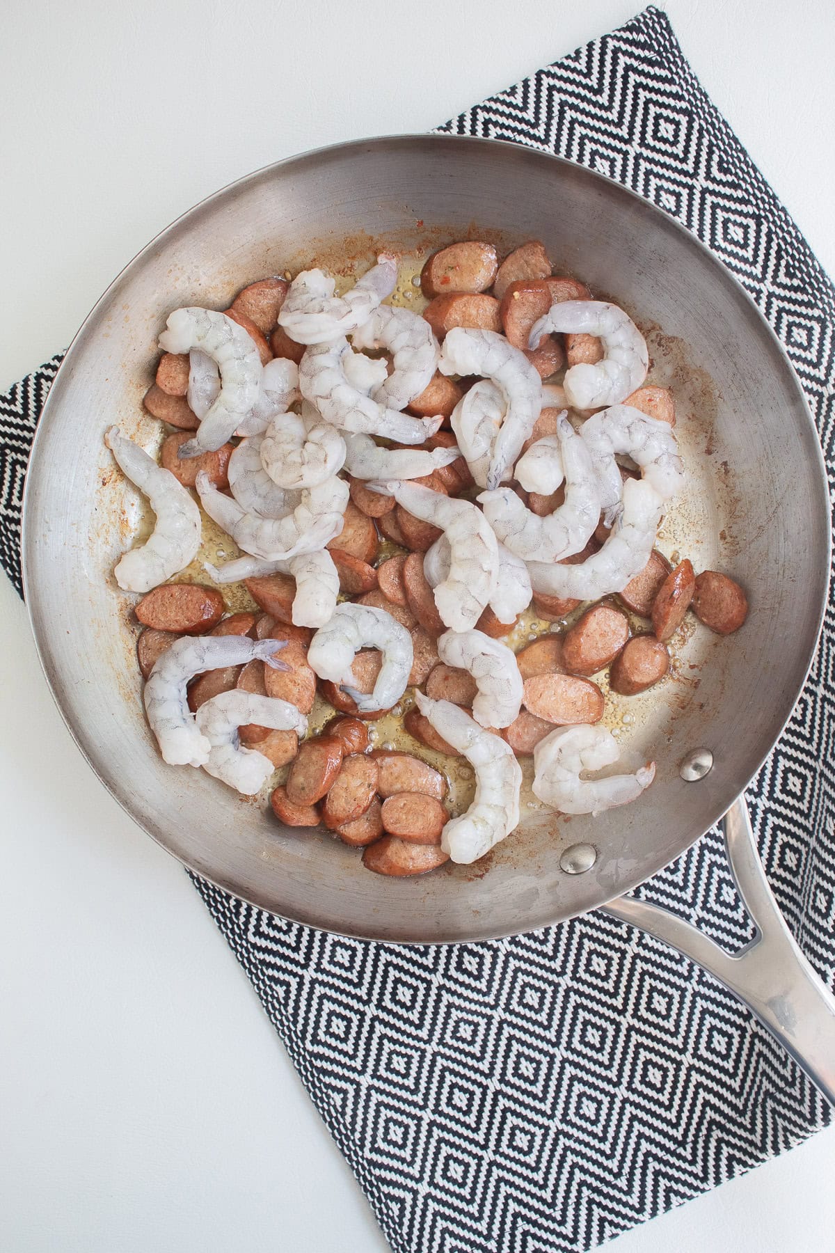 Shrimp are added to the browned sausage in the skillet.