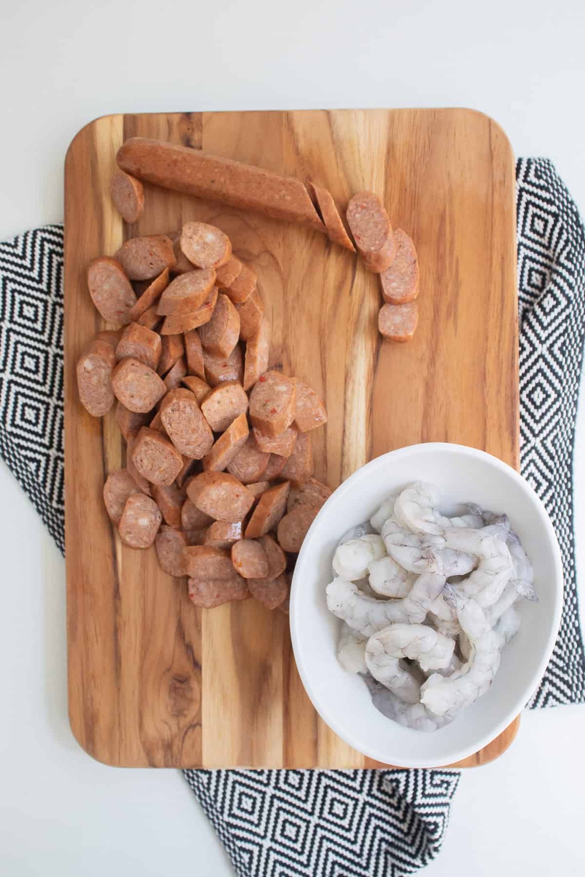 Sausage and shrimp are prepared on wooden cutting board.