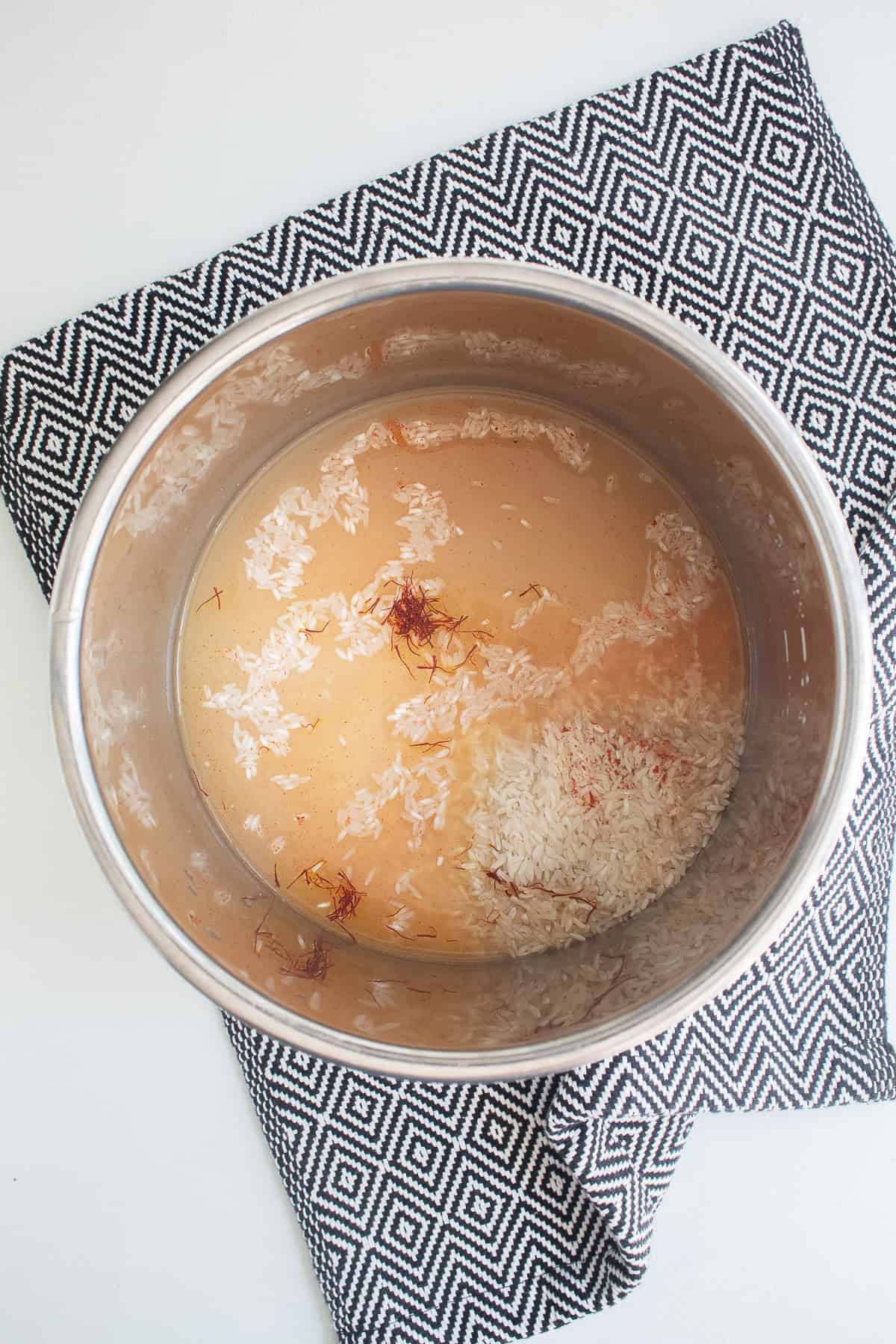 Saffron rice ingredients are added to the insert of a pressure cooker.