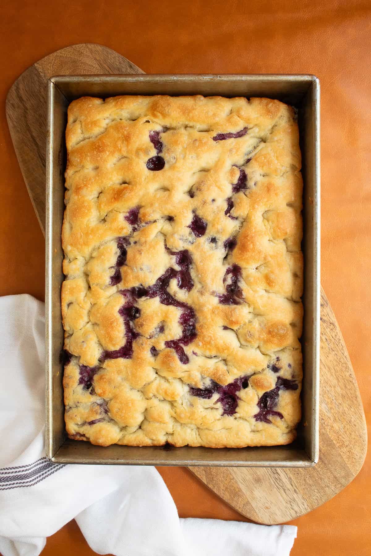 The baked focaccia is golden brown with juicy blueberries peeking through the top.