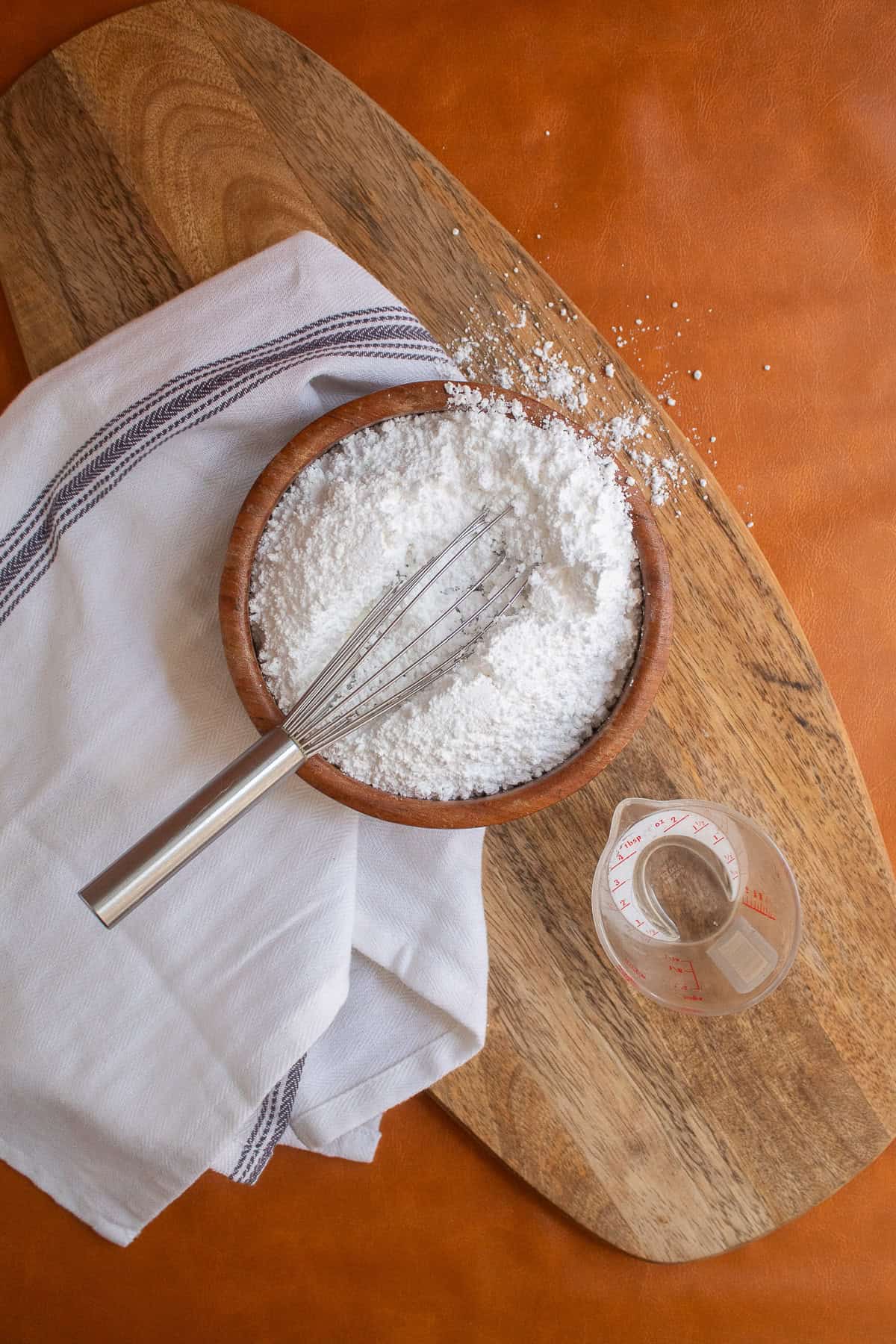 Lemon juice and powdered sugar in a brown wooden bowl are whisked together.