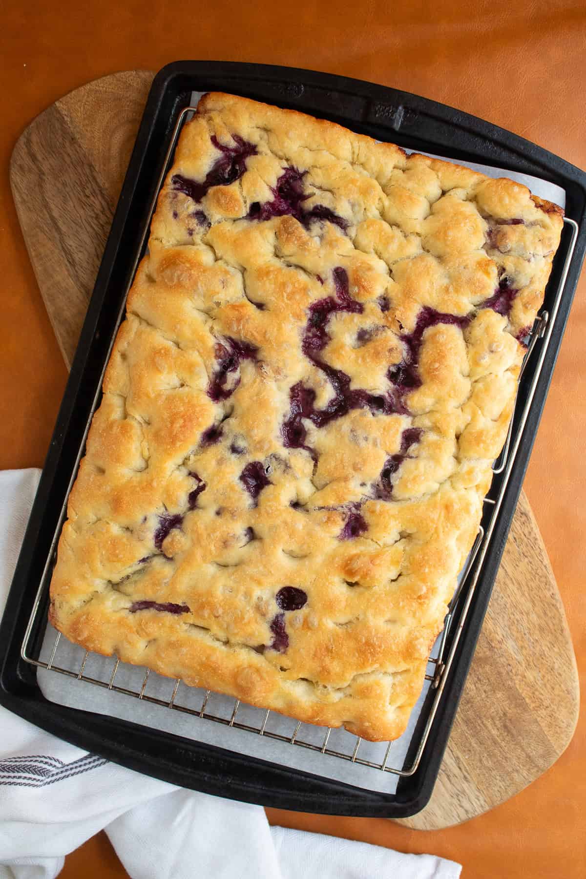 The baked focaccia is transferred to a wire rack over a parchment-lined pan.