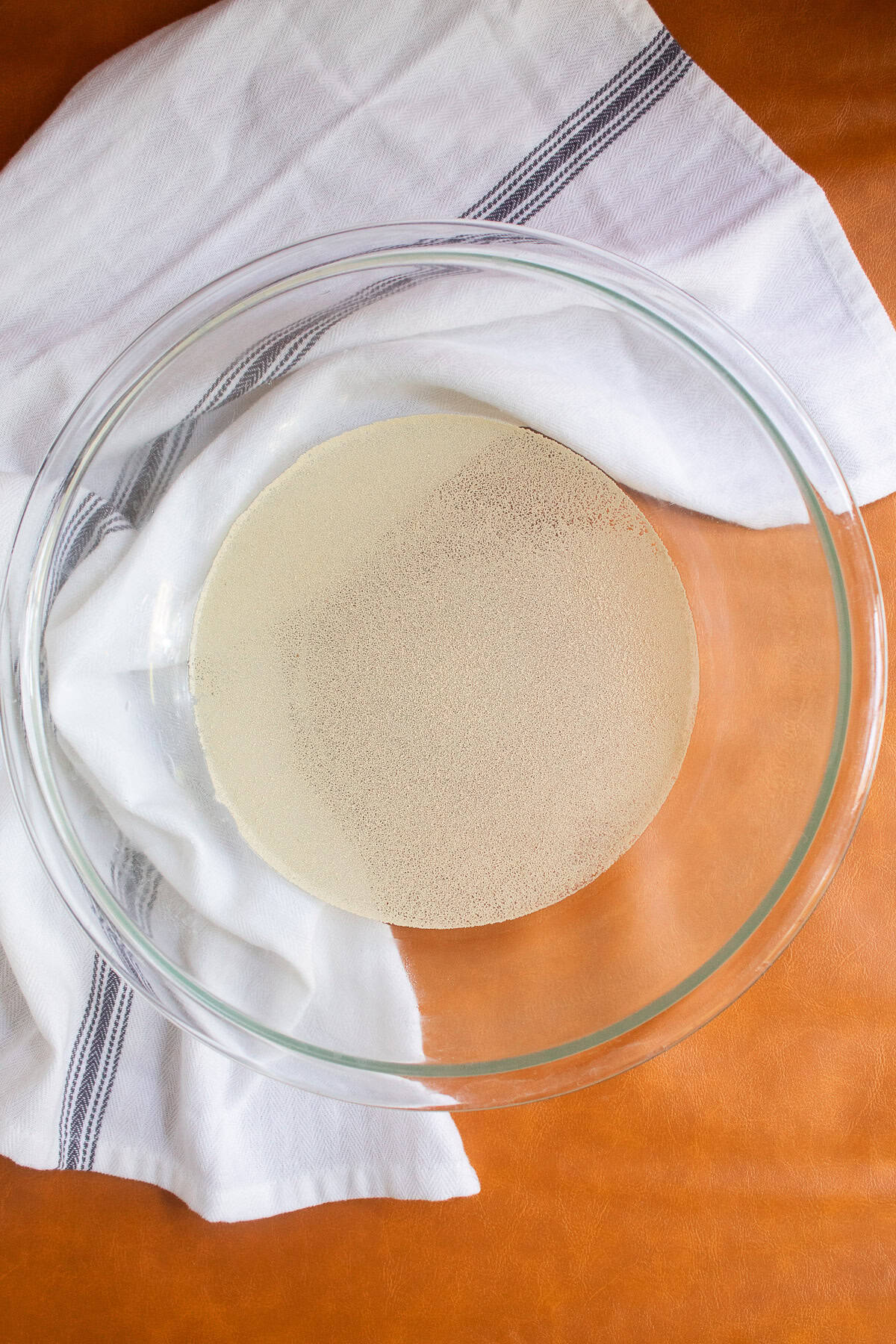 Active dry yeast is sprinkled over water in a large glass bowl.