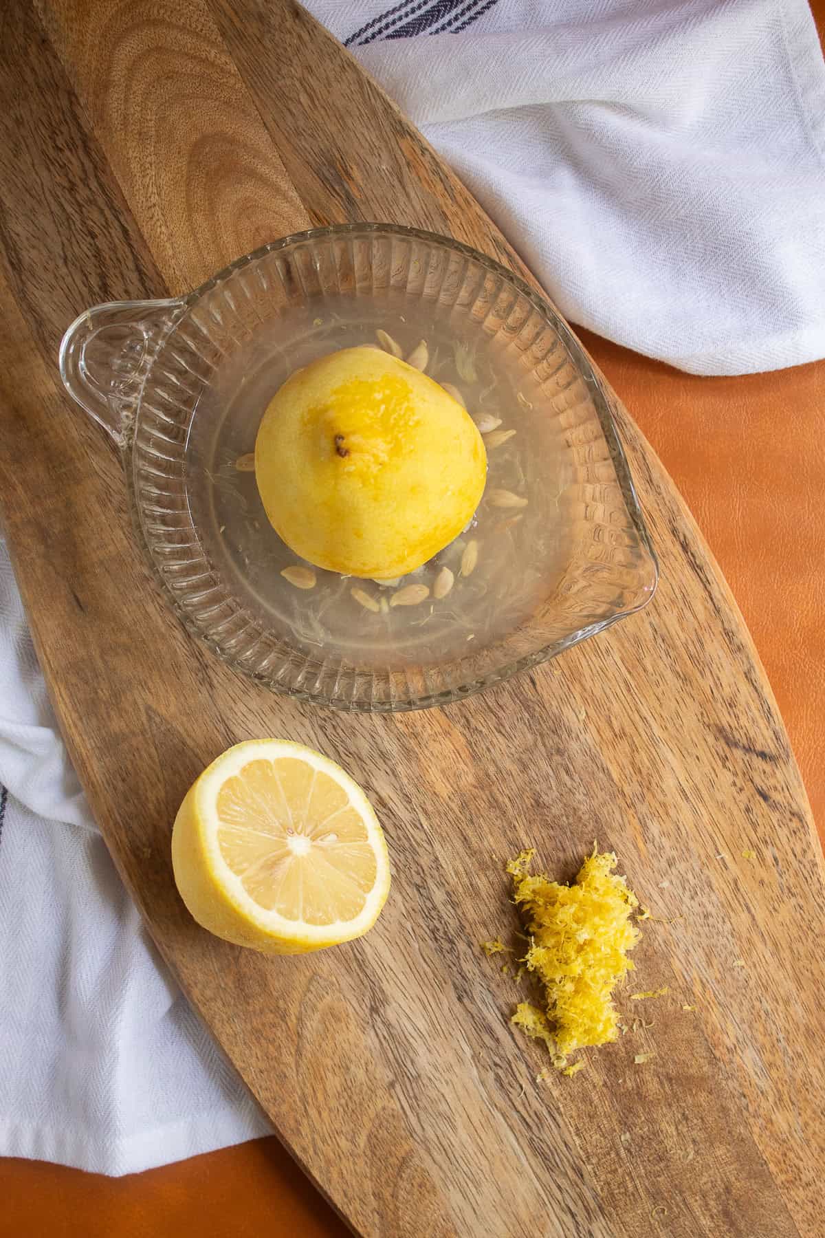 A lemon half is juiced on a citrus reamer next to a pile of lemon zest.