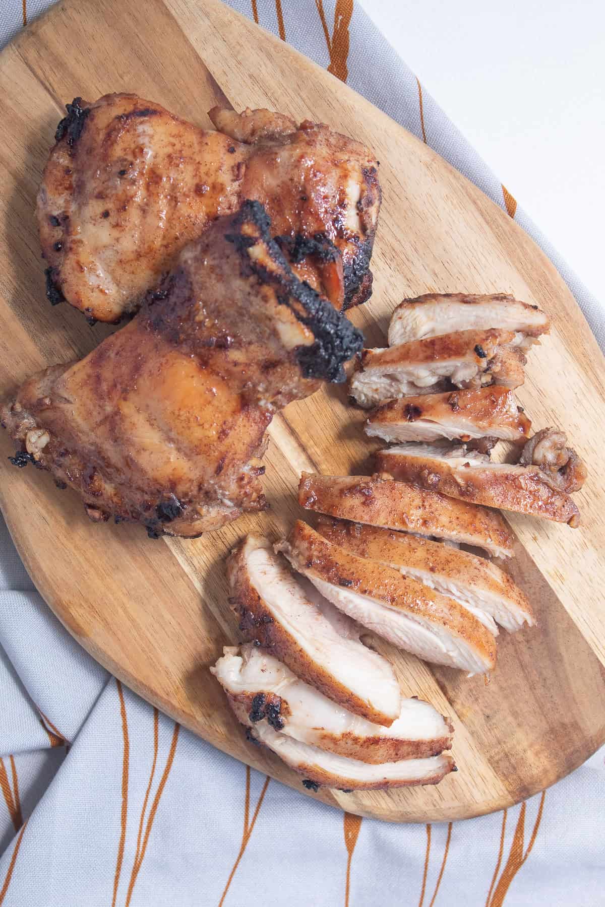 Broiled chicken thighs are sliced on a wood cutting board revealing juicy meat with charred edges.
