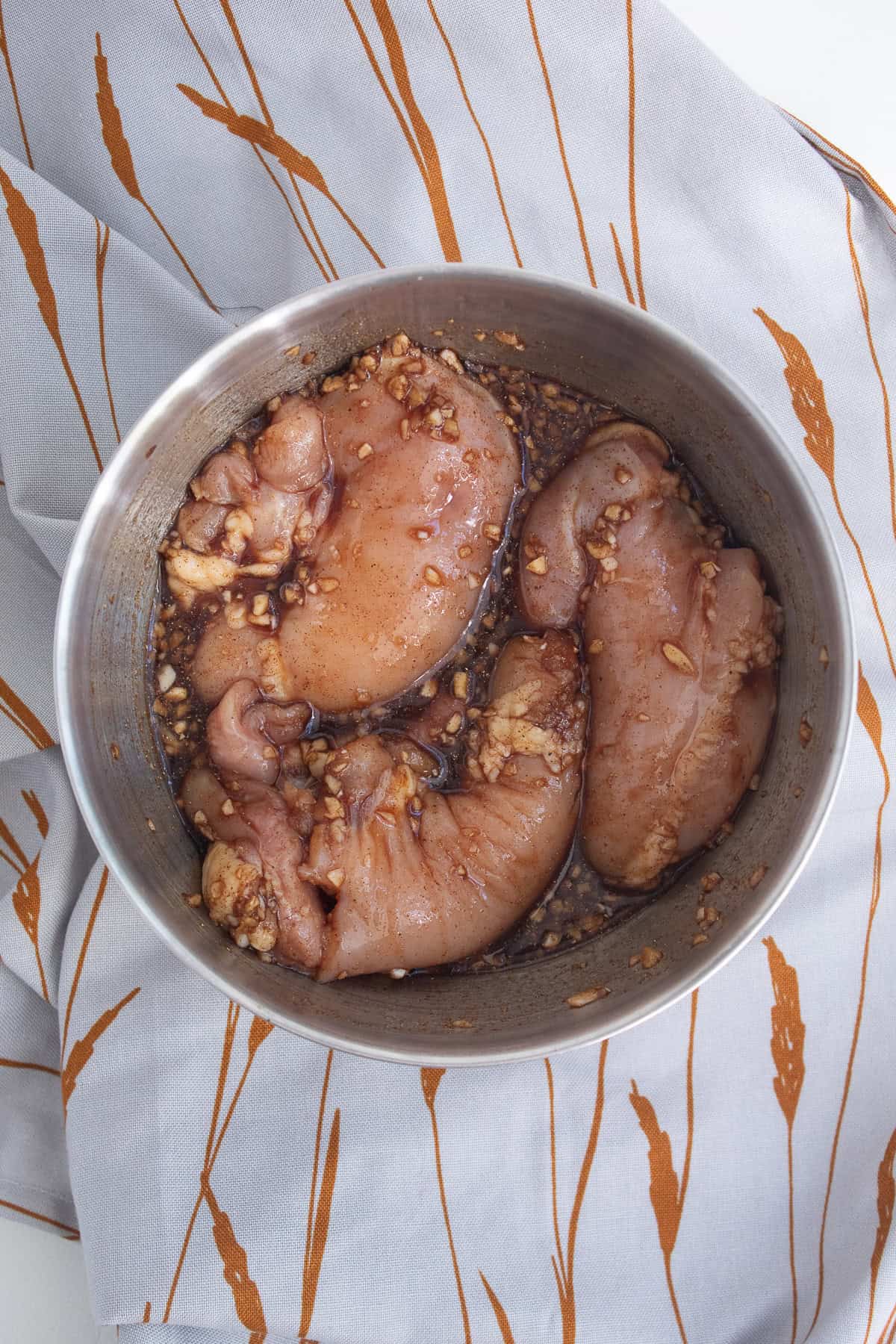 The chicken thighs are well coated in marinade in a medium bowl.